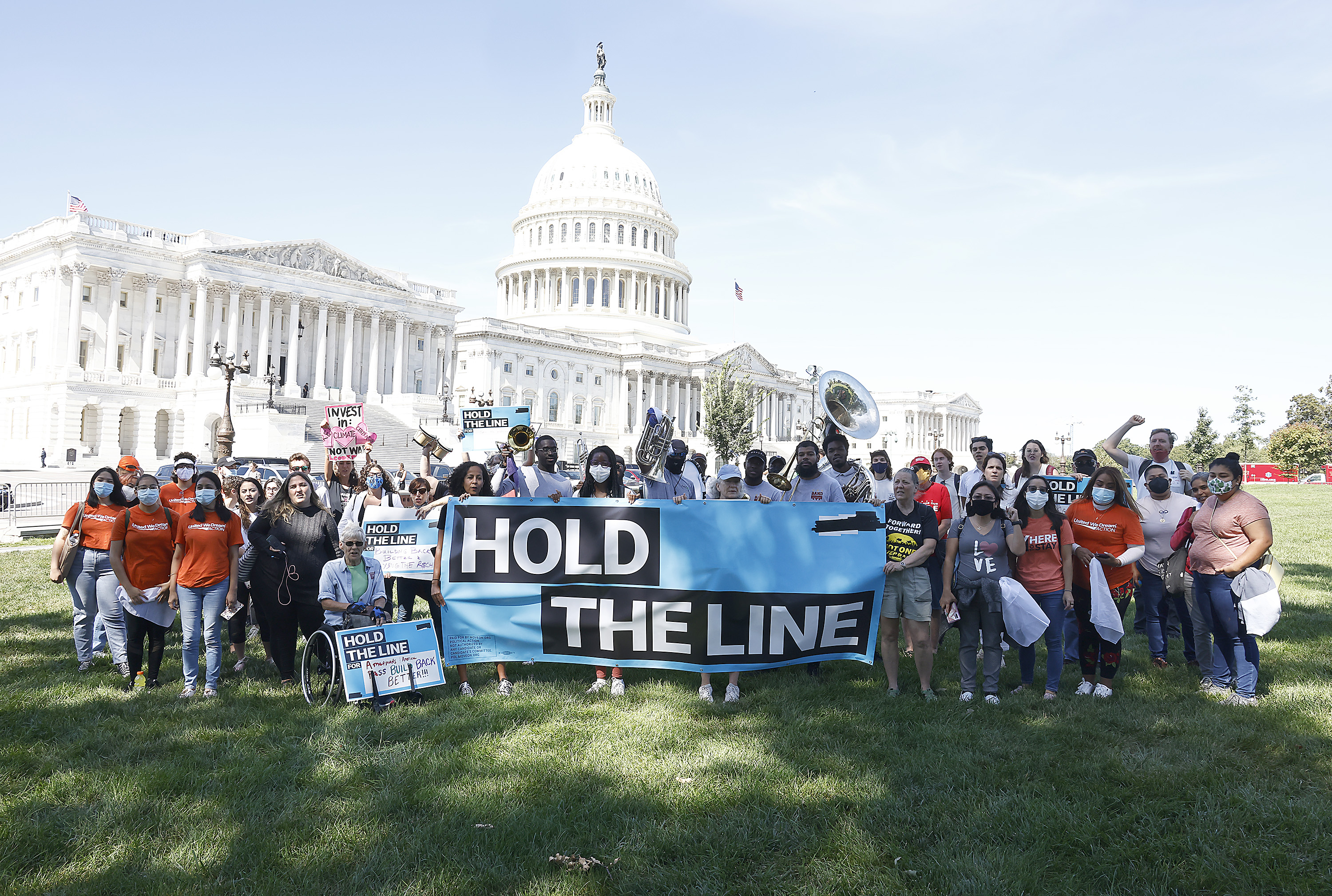 Demonstrators stand on the lawn in front of the US Capitol holding a banner that reads “hold the line.”