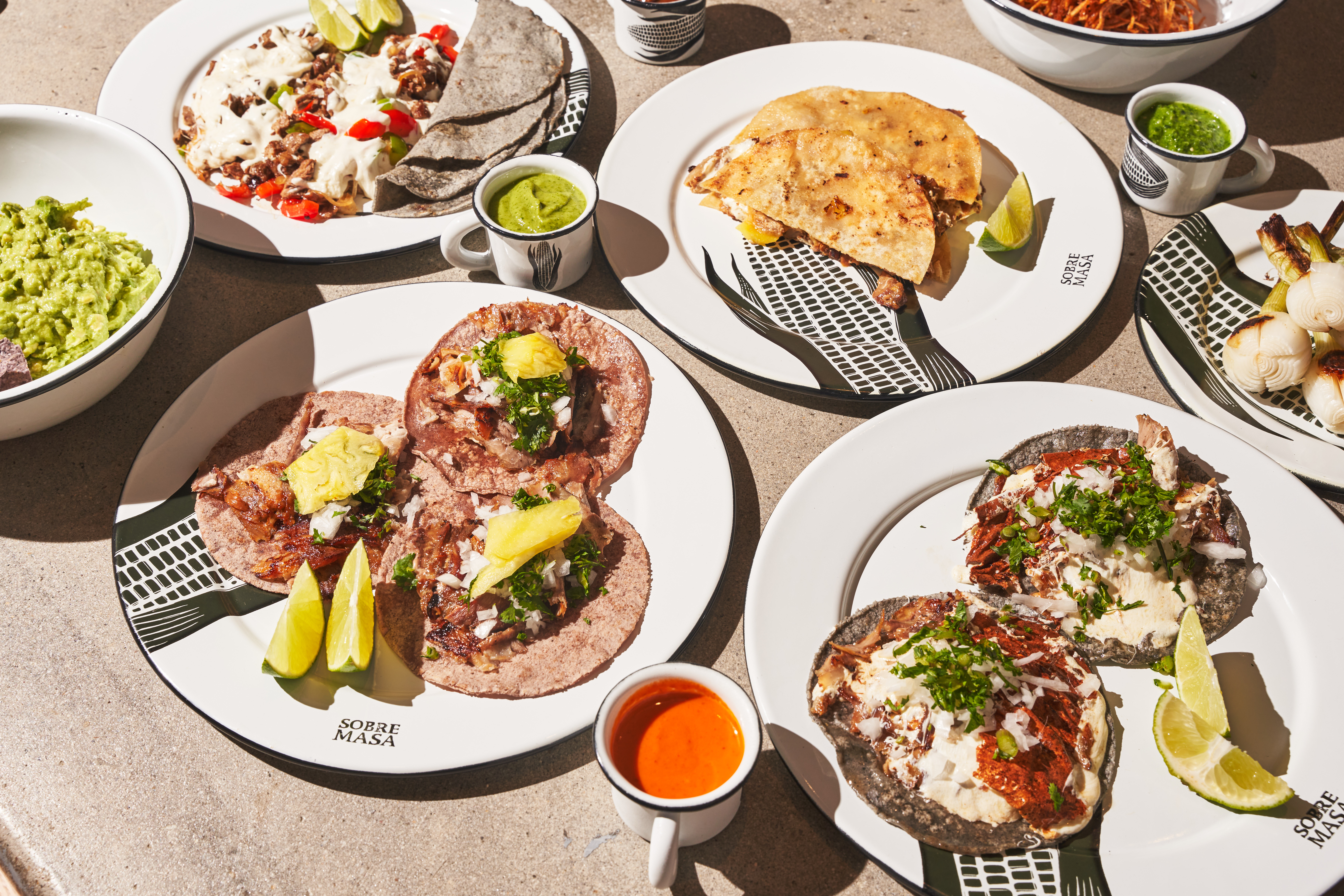 An assortment of tortilla dishes, including tacos and gringas, topped with meats and cheeses.