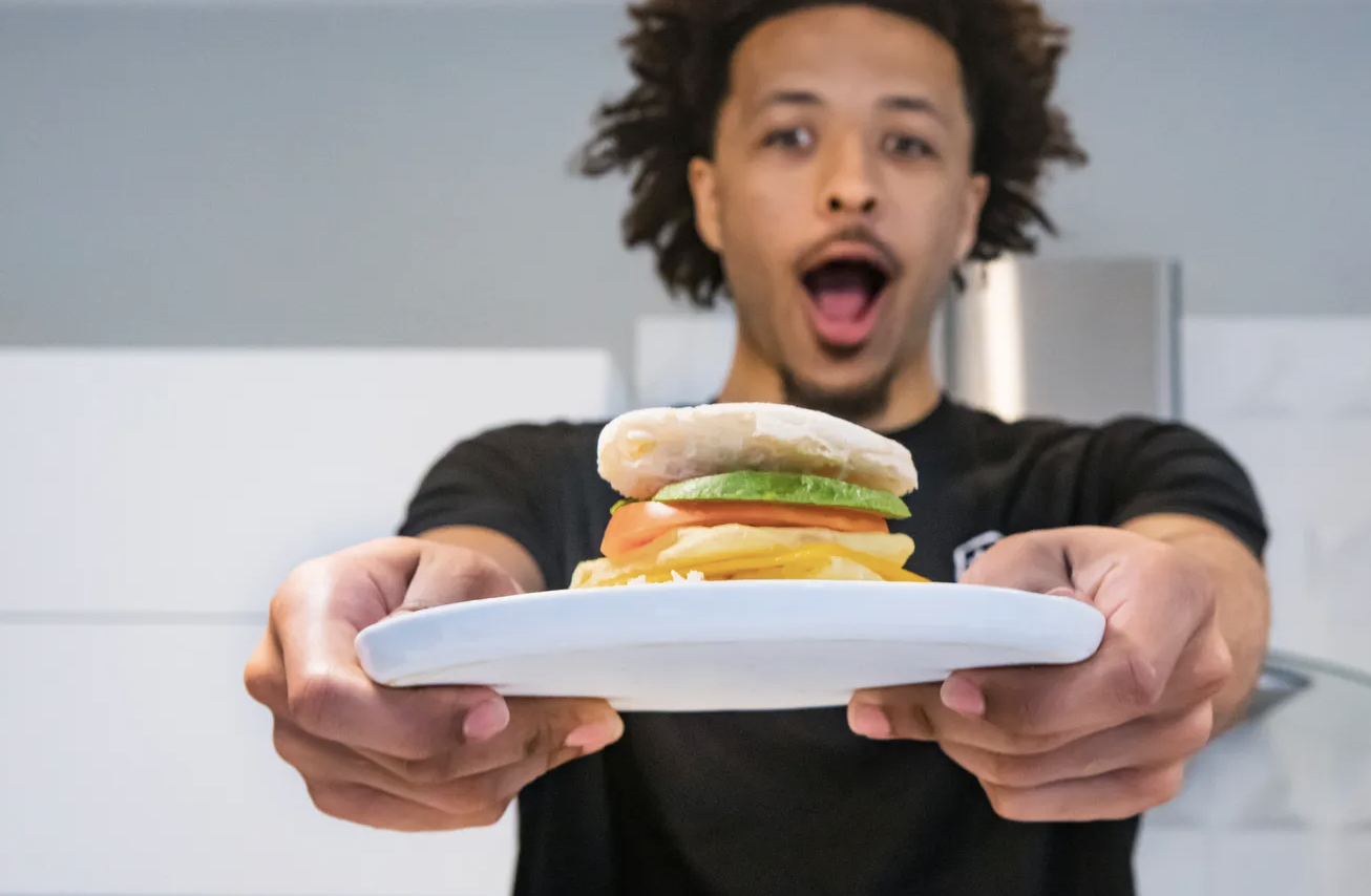Cade Cunningham holds a sandwich on a plate with arms stretched toward the camera