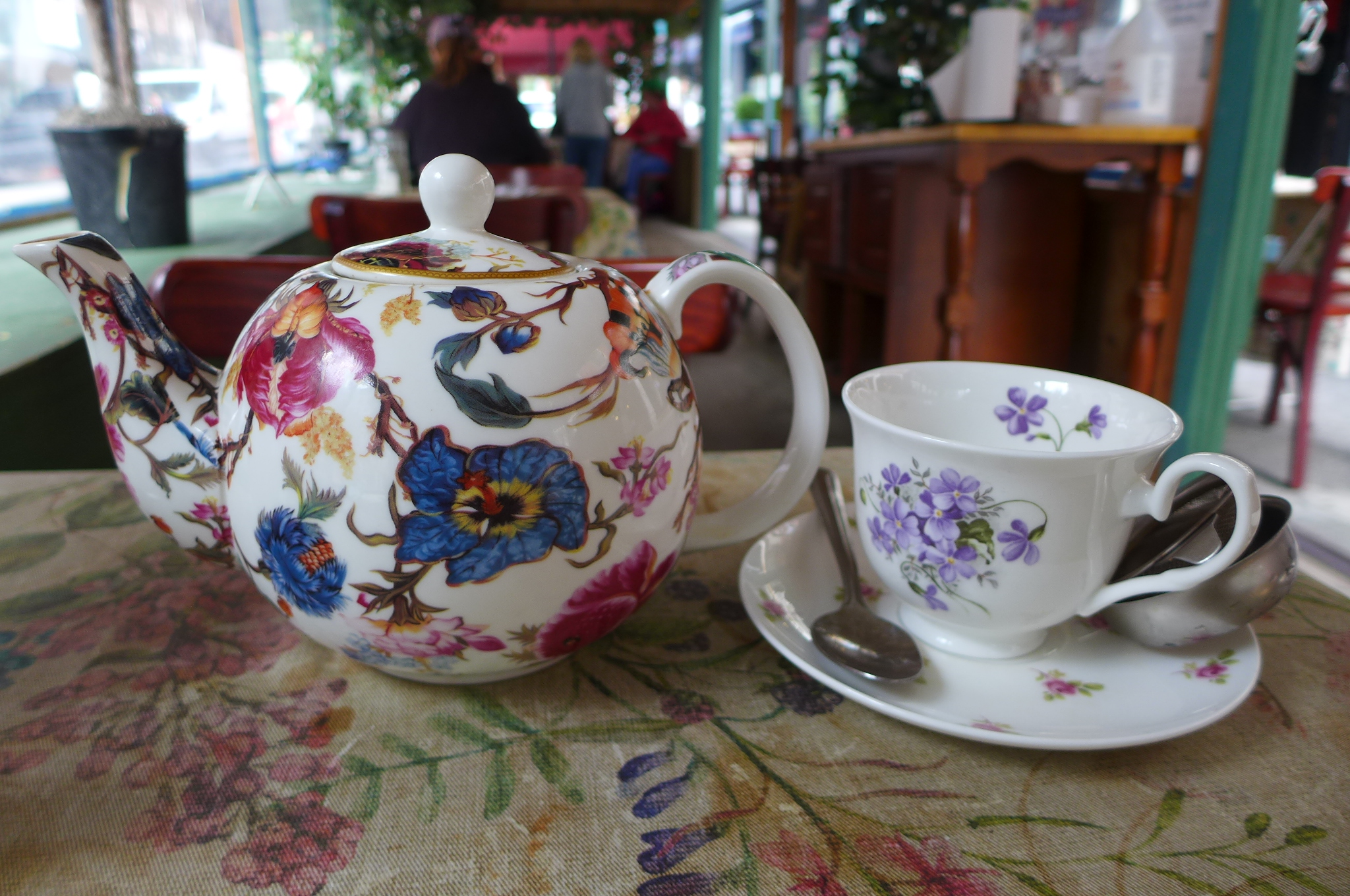A flowered tea pot with a matching teacup on the side.