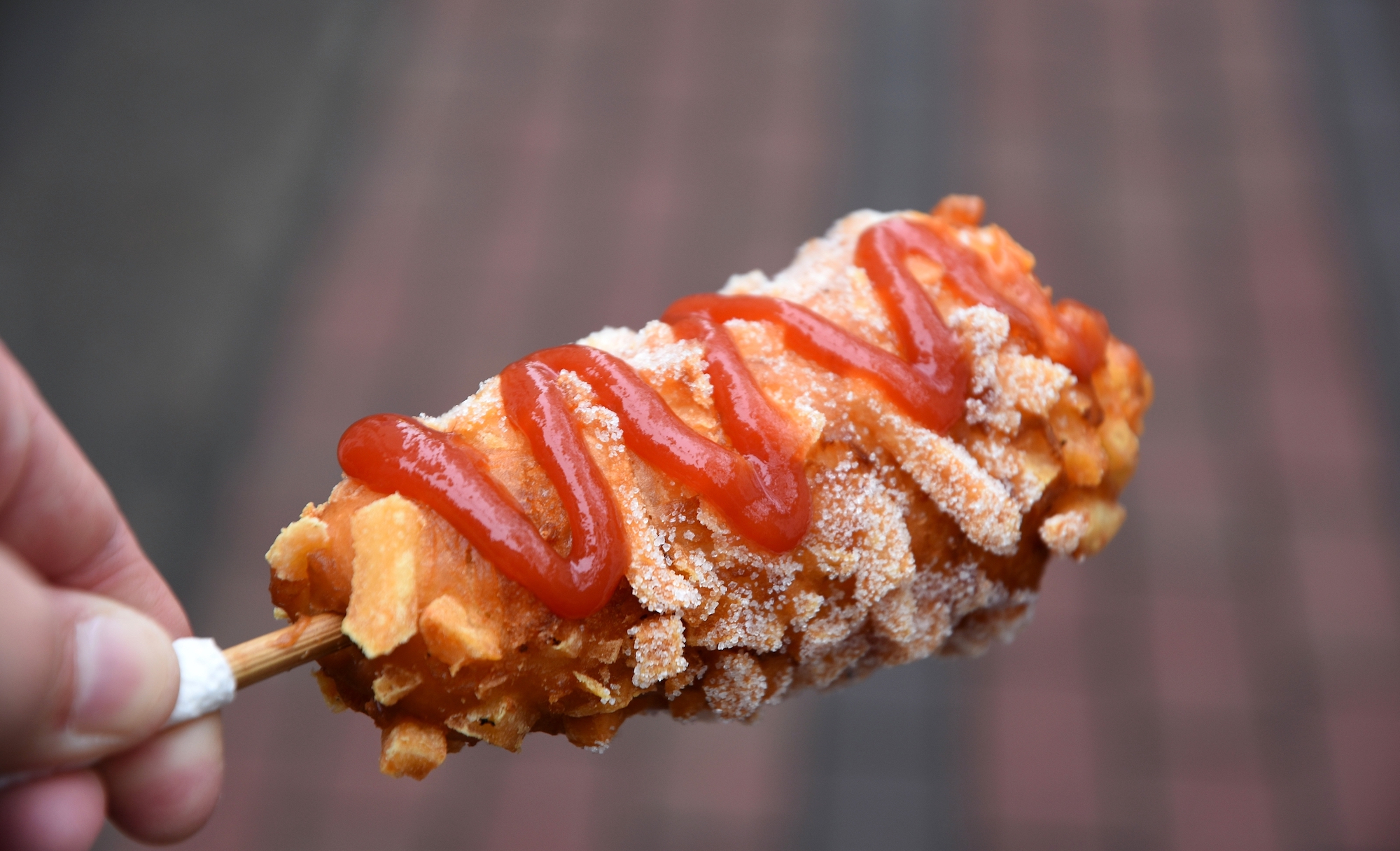 A hot dog on a stick covered with french fries and a squiggle of ketchup