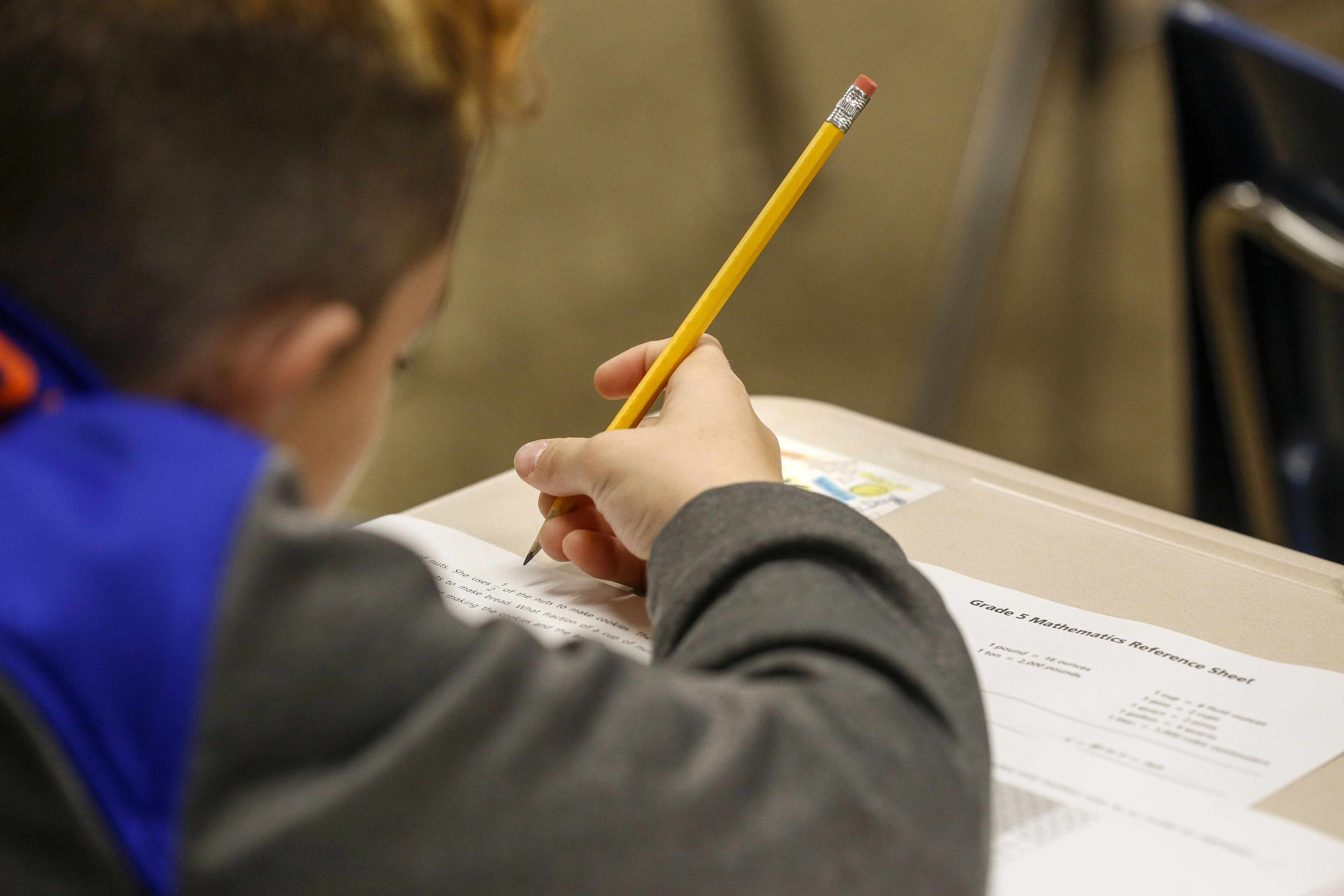 A student takes a test at their desk, writing with a number two pencil.