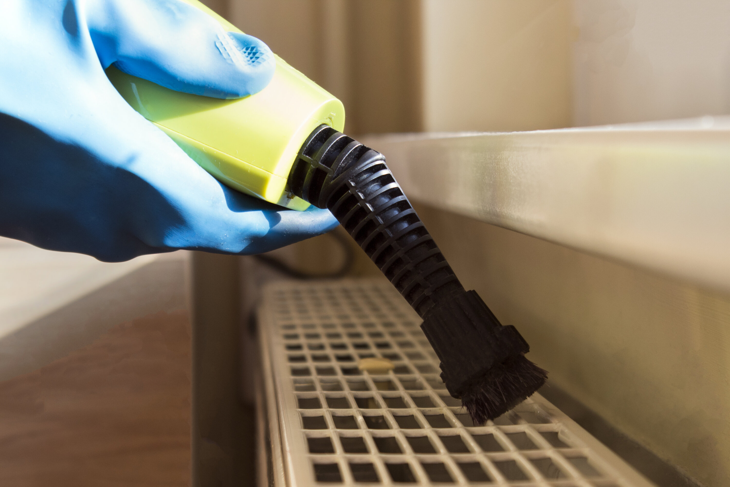 A person with a blue protective glove holding a yellow and black fumigation device spraying it into a radiator 