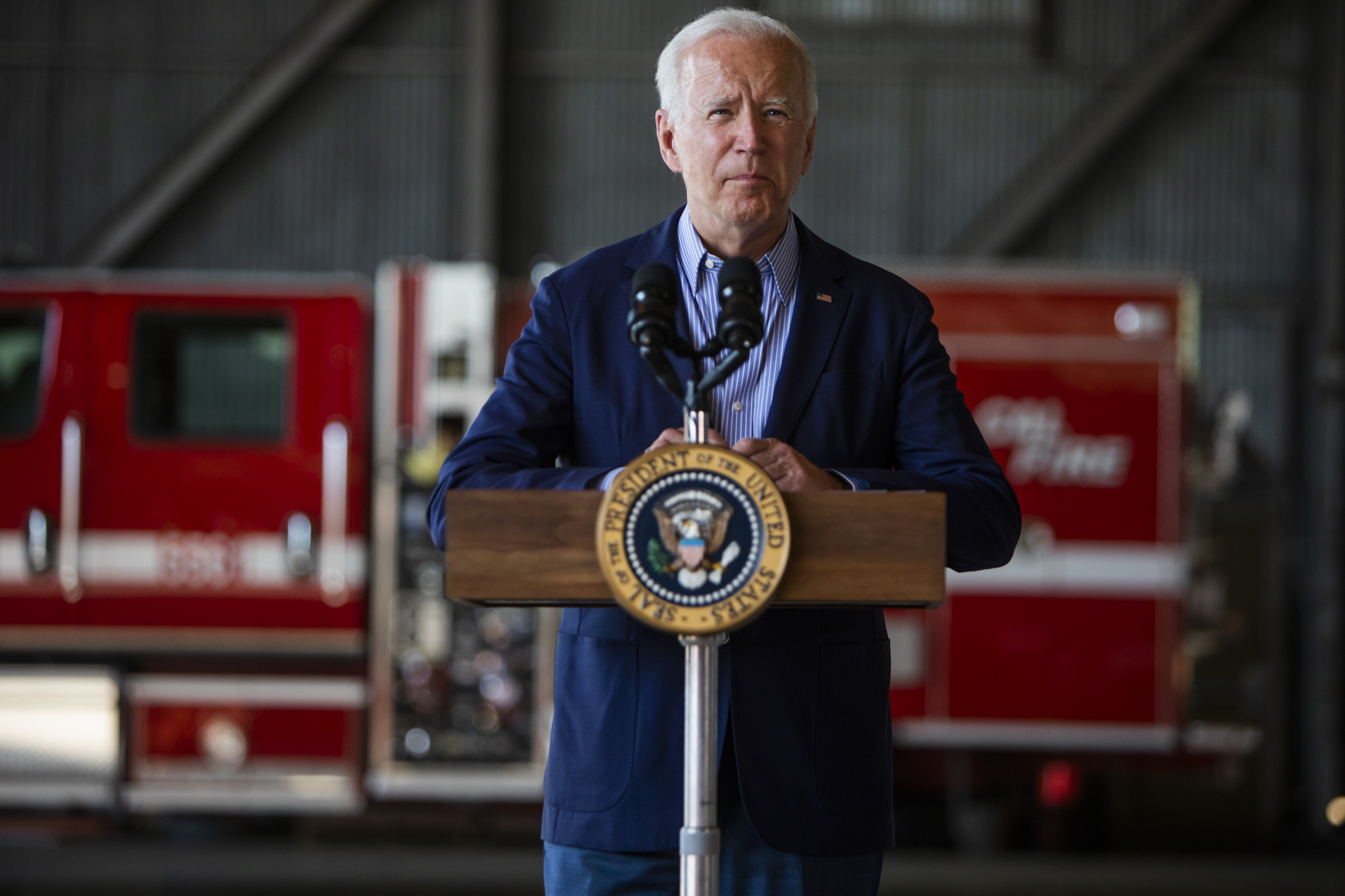 President Biden stands and speaks from a lectern set up near a red emergency vehicle.