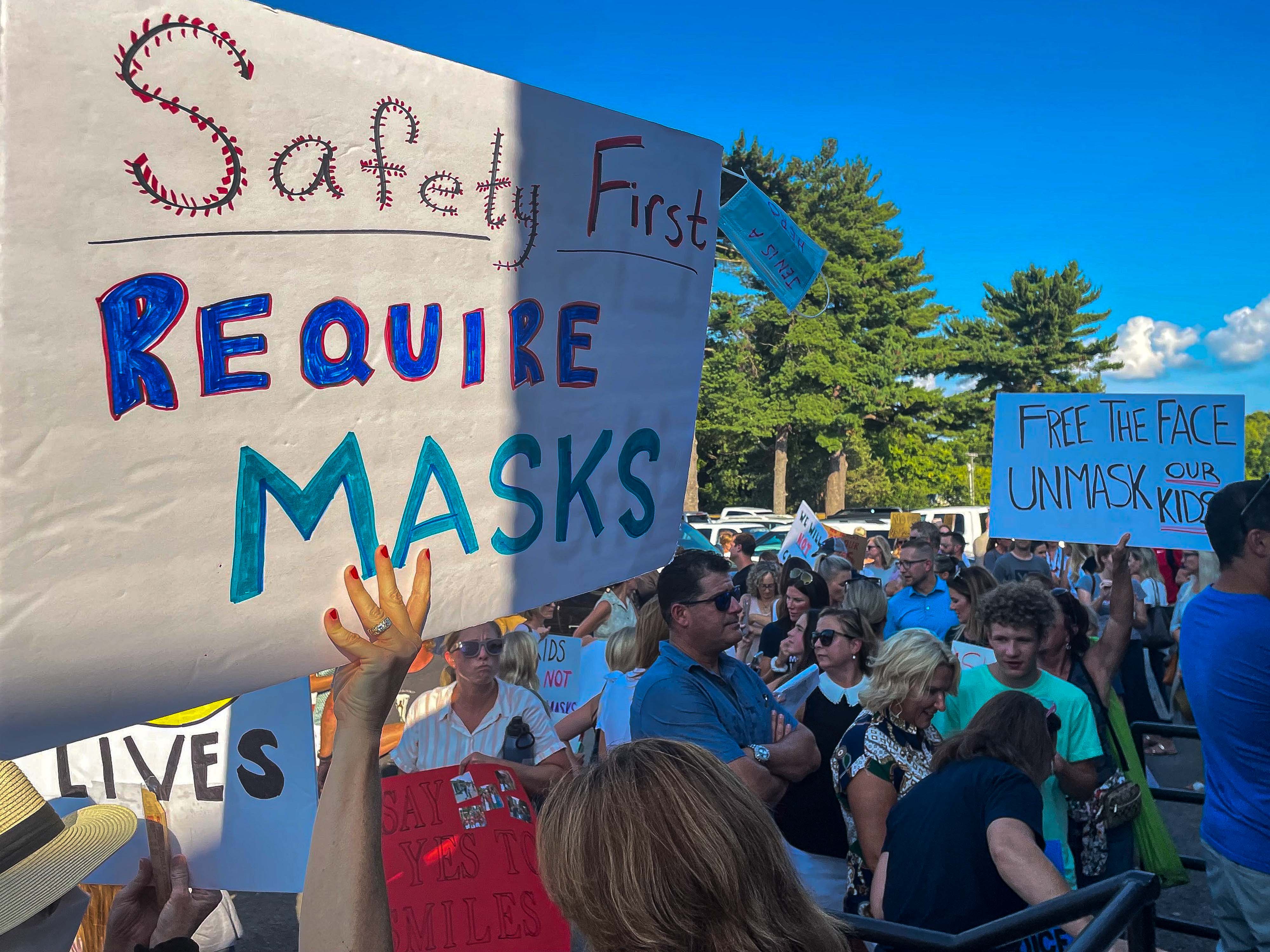 A crowd of people hold up signs for and against school mask mandates during a daytime protest.