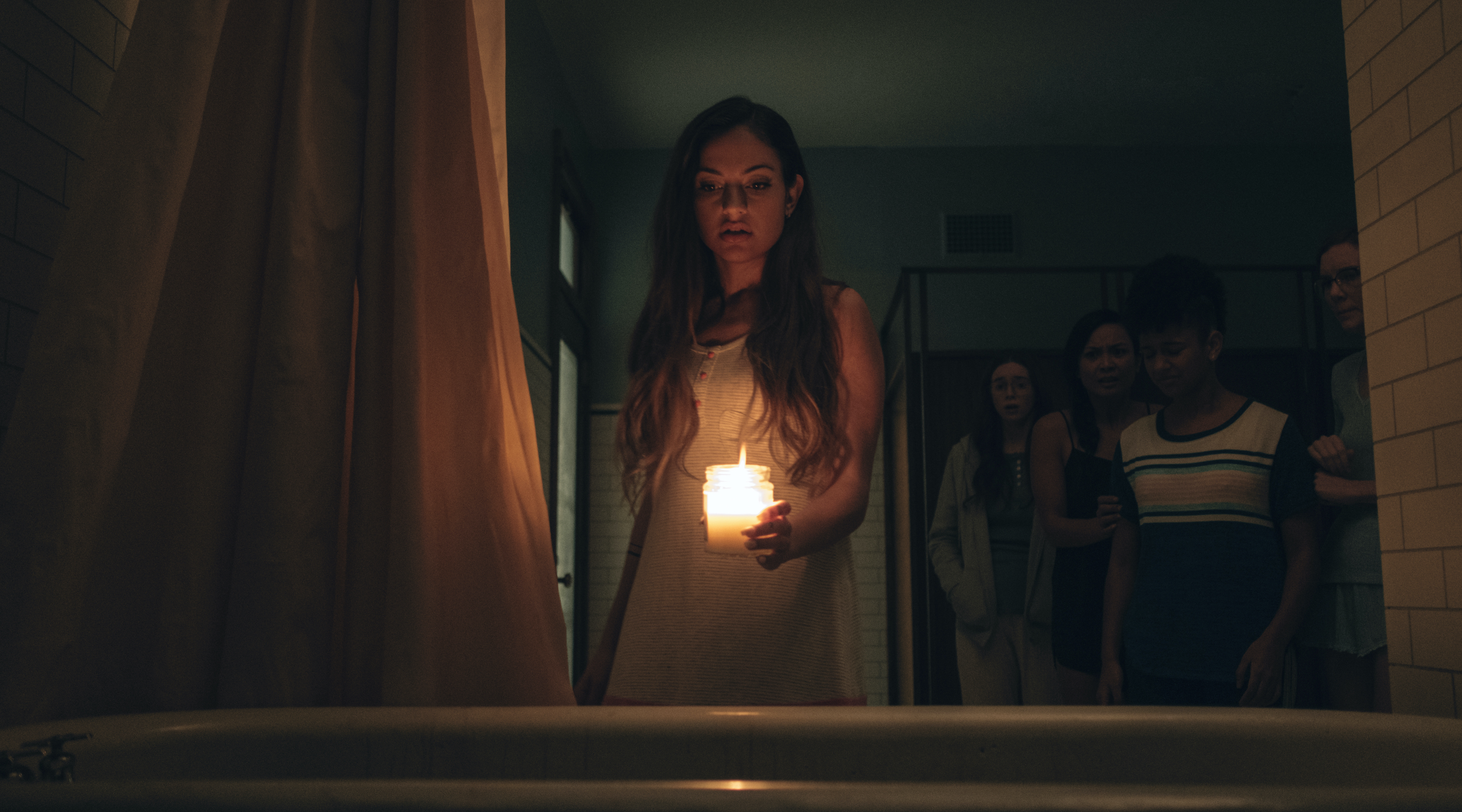 Inanna Sarkis as Alice holds a candle over a bathtub in a darkened bathroom in Seance