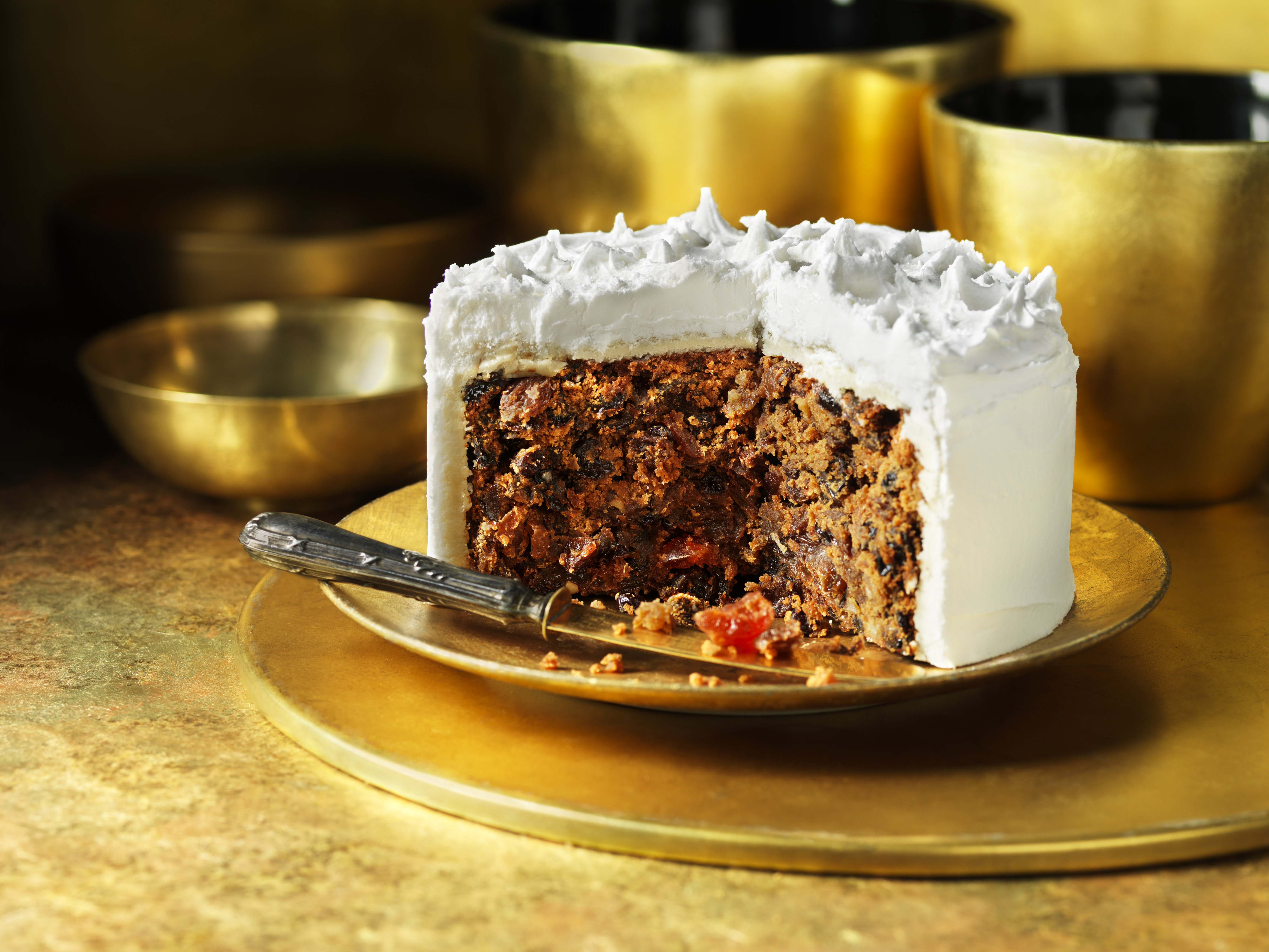A Christmas fruitcake covered in white icing, sliced open on a gold plate.