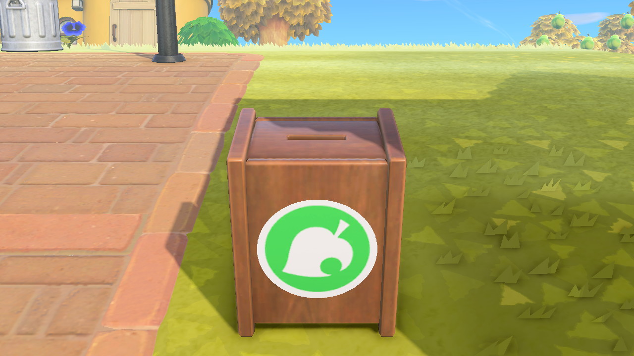 A wooden box with the Animal Crossing leaf logo sits on a grassy area next to a tiled area.