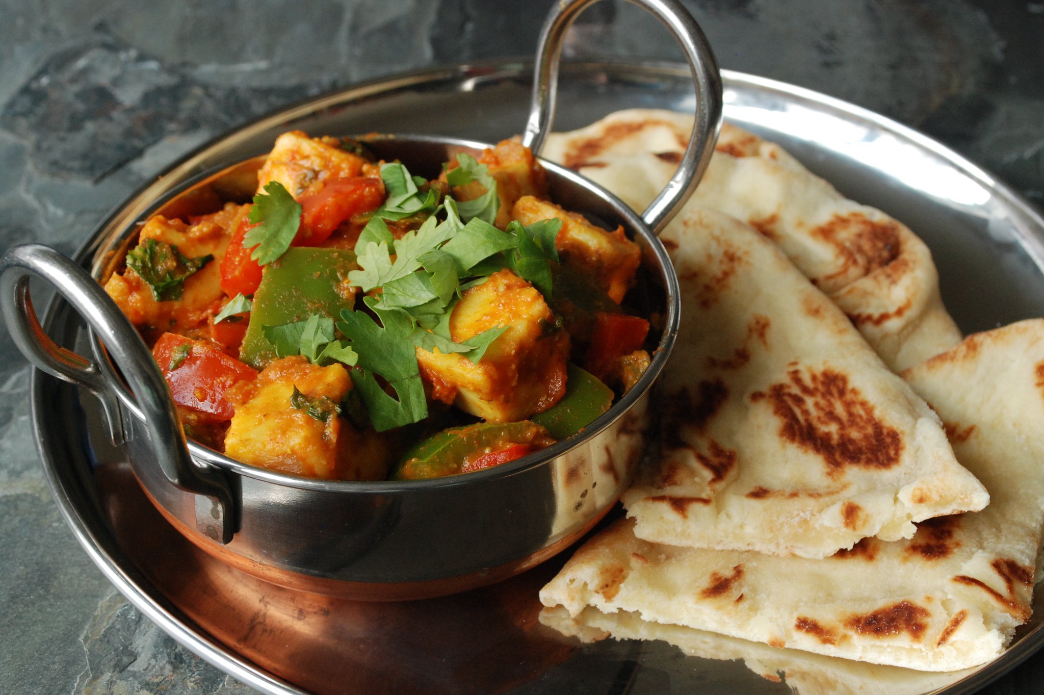 A side angle photo of Indian paneer dish in a metal tray on a stone table.