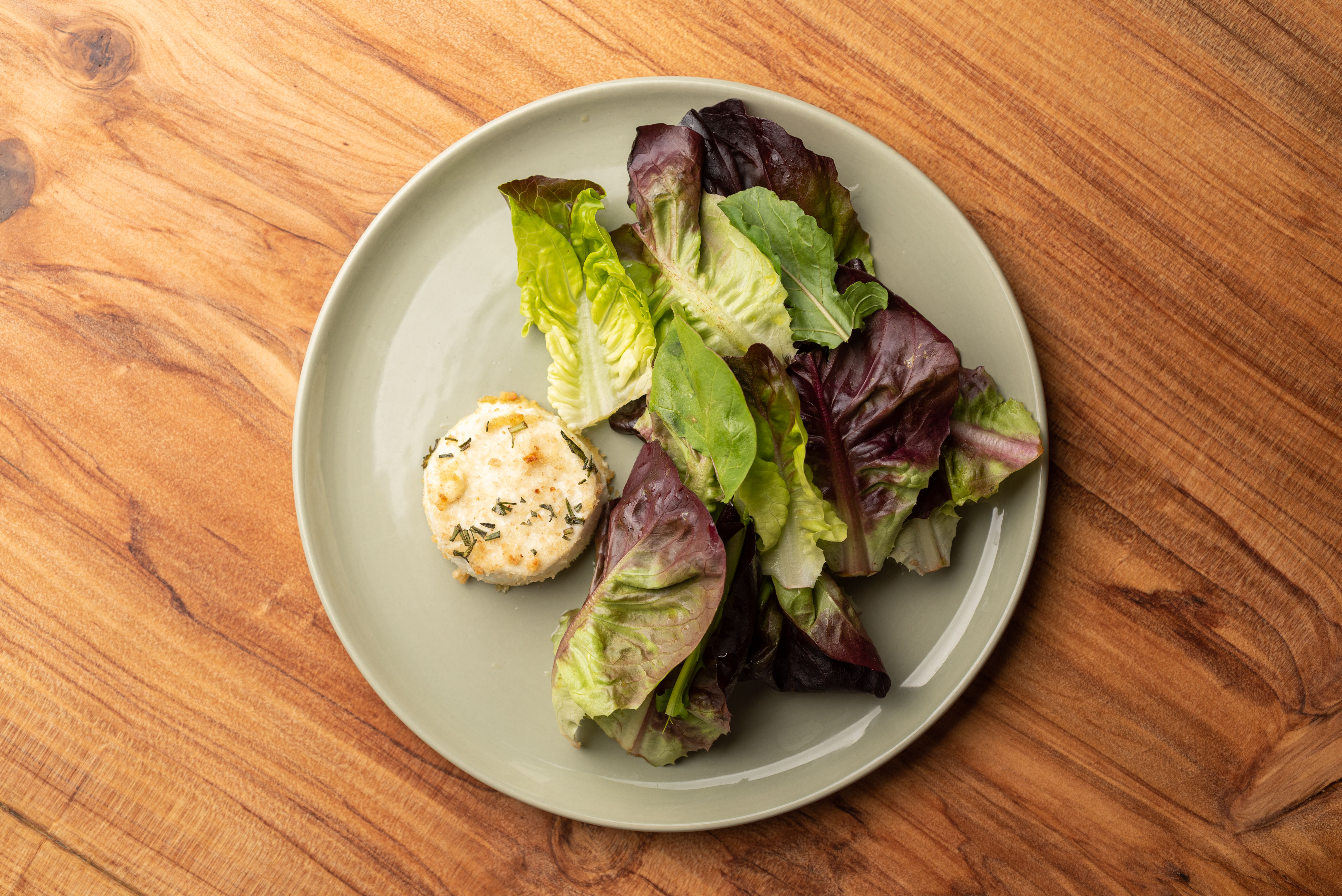 An overhead shot of a simple plate of lettuces and ring of baked goat cheese during daytime.