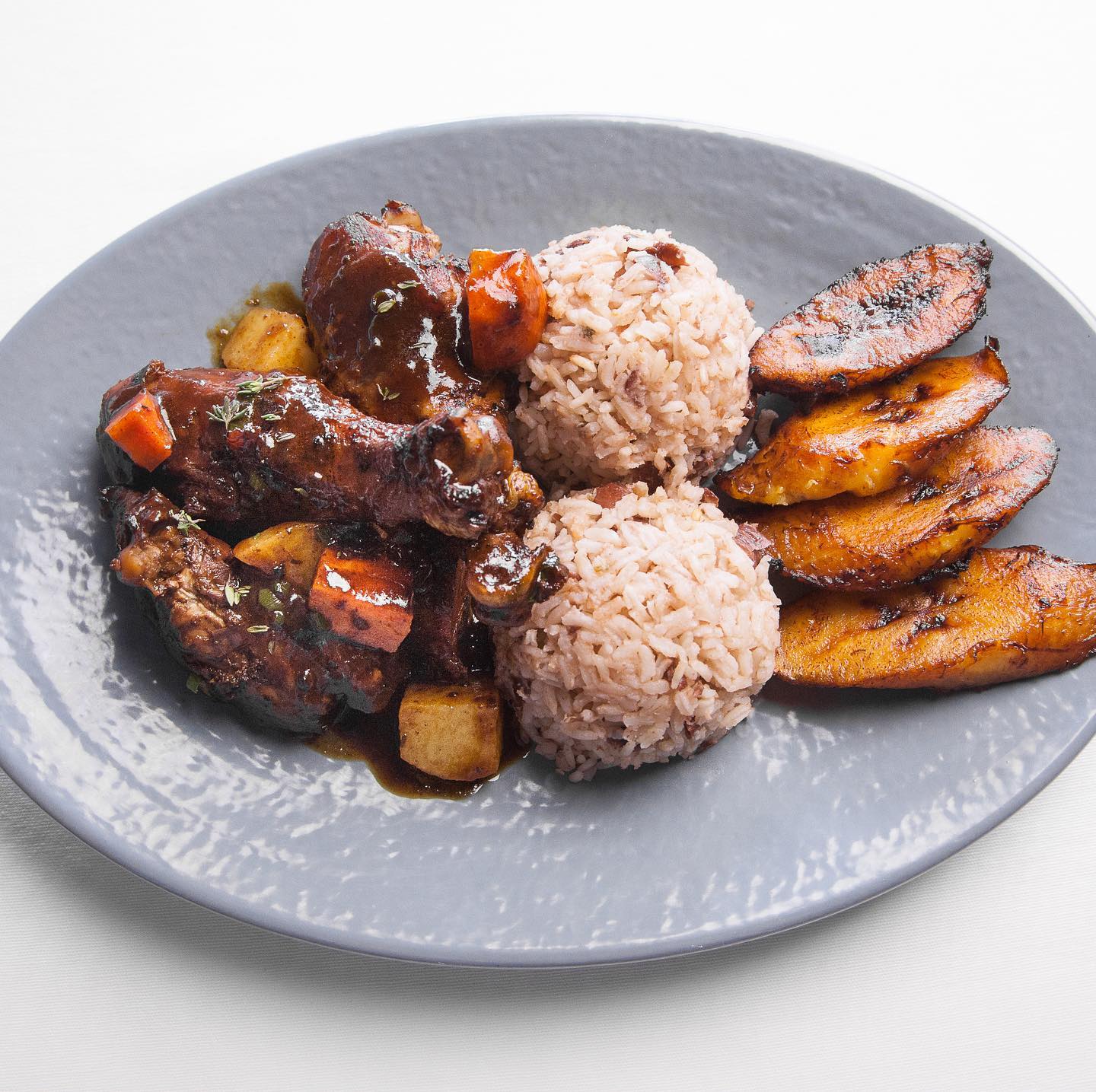 Jamaican style brown stew chicken served with rice and peas and fried plantains.
