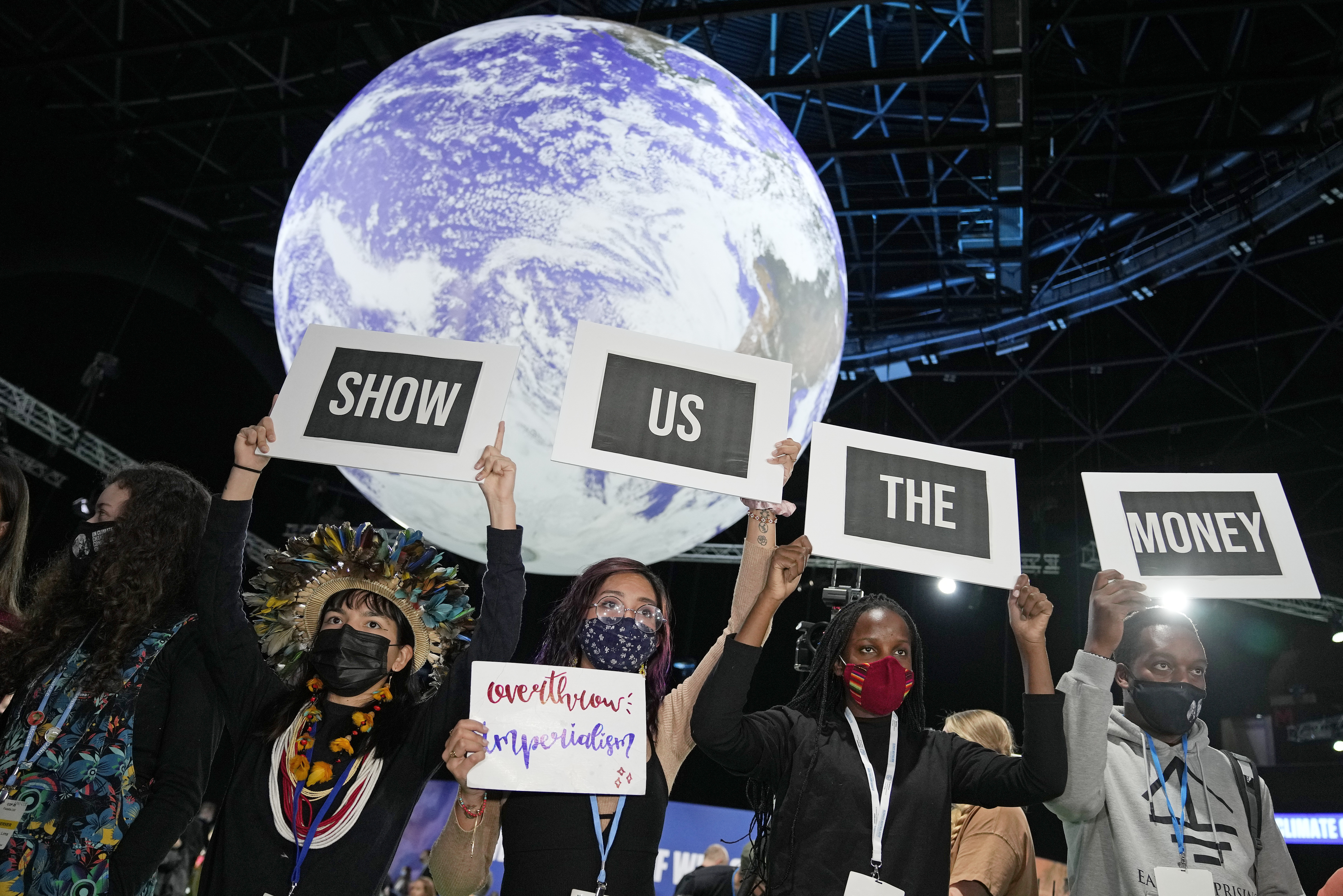 Masked protesters outside of the UN climate talks in Glasgow, Scotland, hold signs that read “SHOW US THE MONEY”