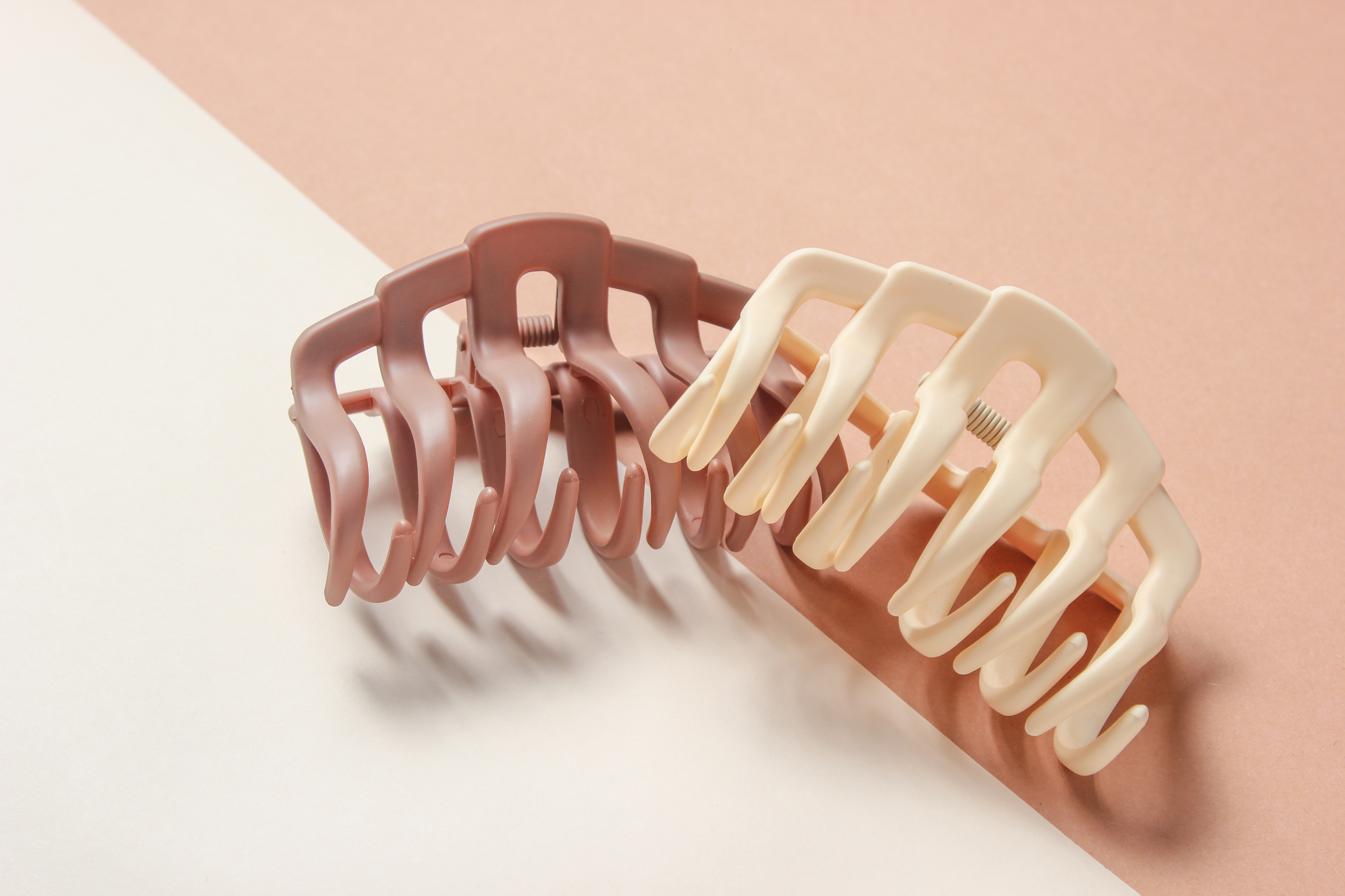 Two claw clips, one blush pink and one alabaster white, against a pink and white background.