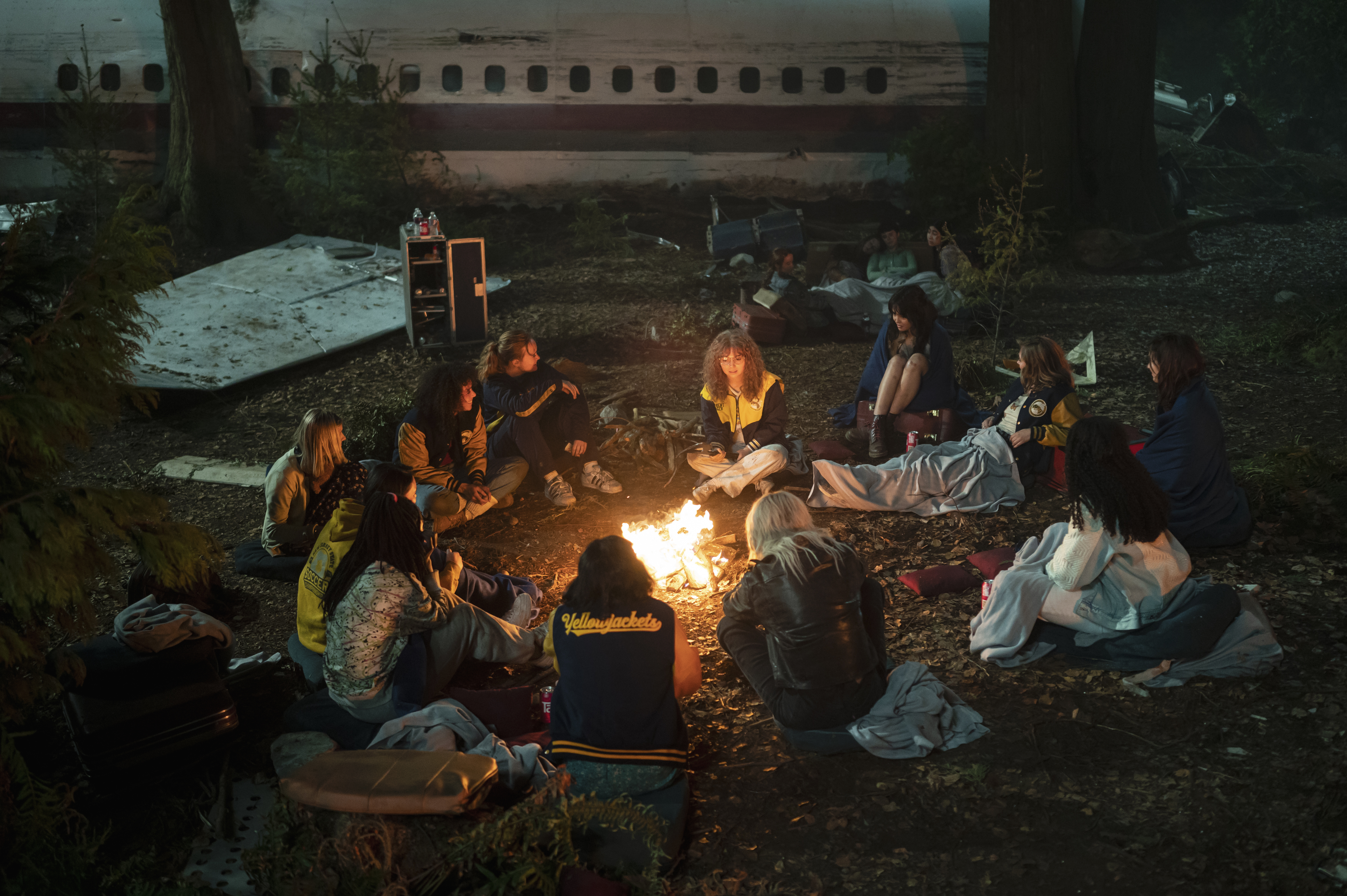 A campfire provides warmth for the plane crash survivors in a wide shot.