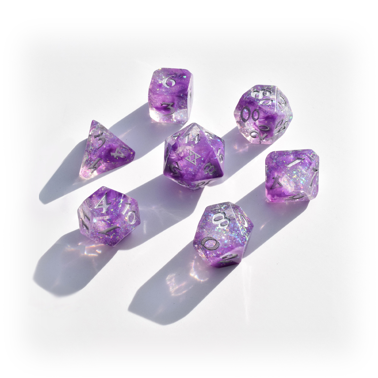 Image of a seven dice set: a D4, D6, D8, D10, D12, D20, and D100. The dice have a galaxy swirl inside them of dark purple, light purple, and clear with iridescent glitter flakes. The numbers are painted silver. The D20 has the BoB sigil on the 20 side.