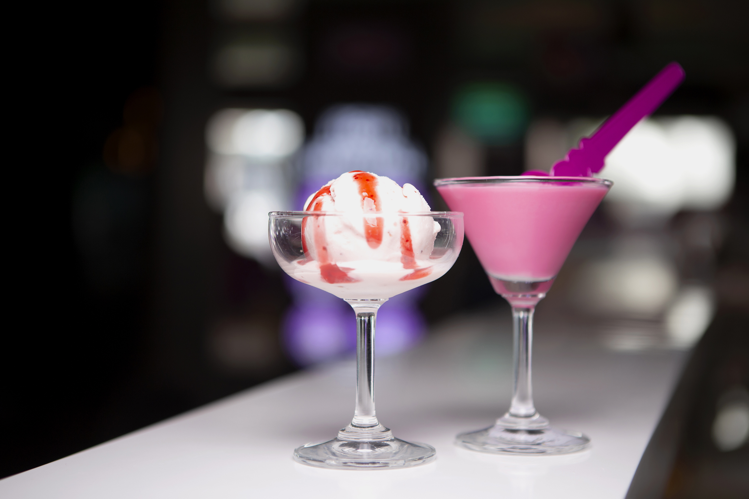 A scoop of vanilla gelato in a glass next to a pink-colored cocktail.
