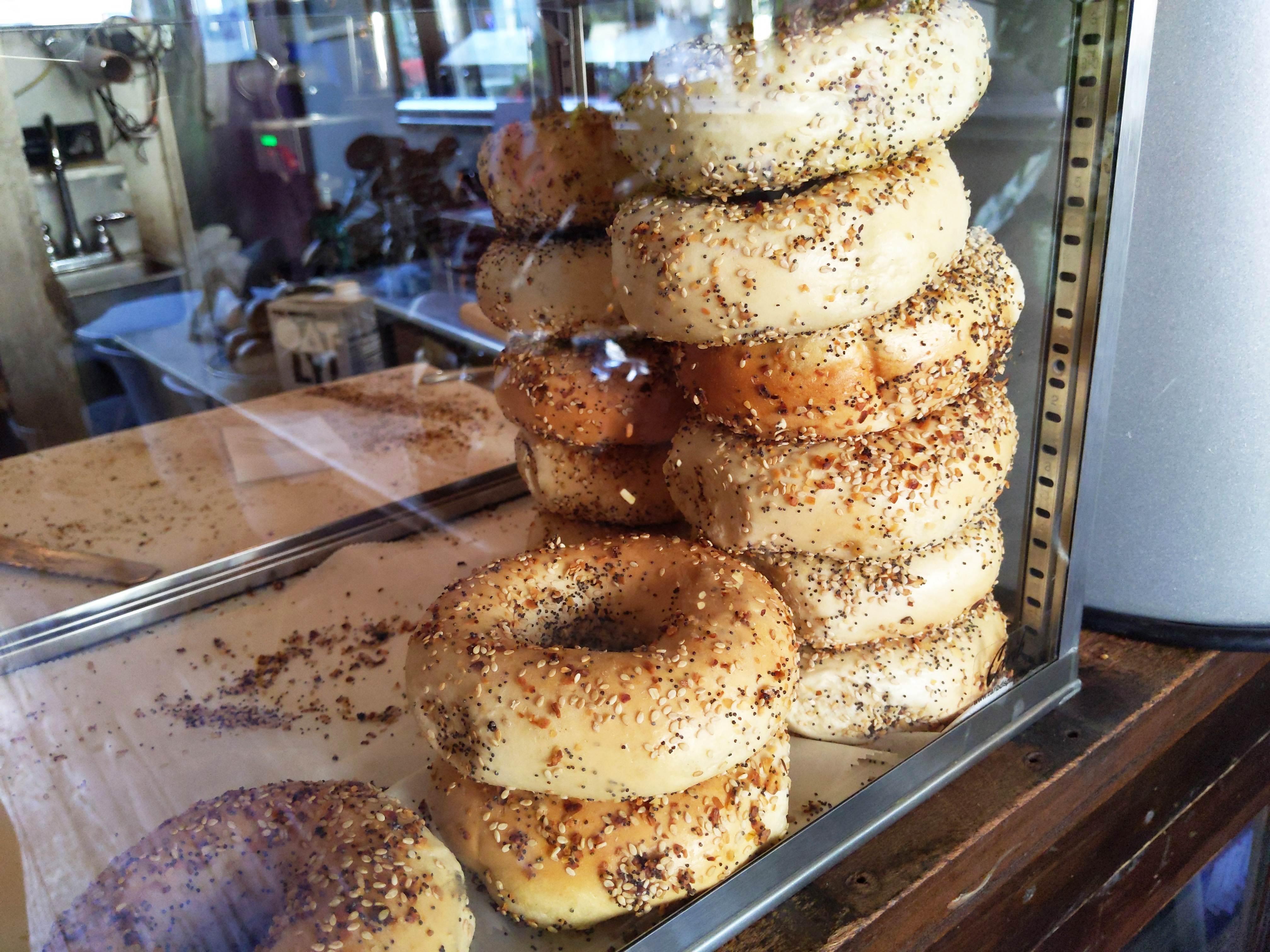Several stacks of everything bagels in a plexiglass case.