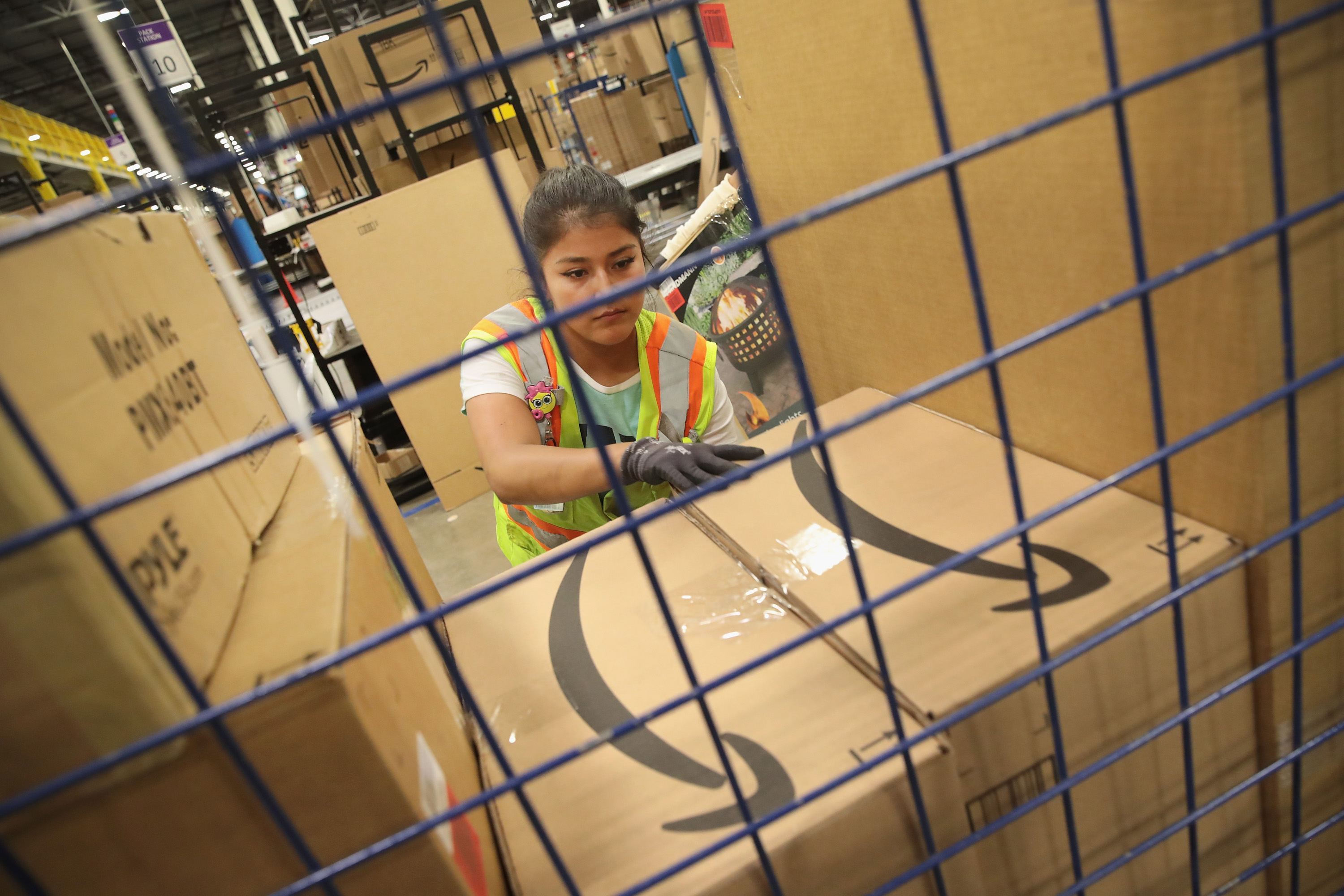 A worker in a safety vest stacks Amazon boxes higher than their head.