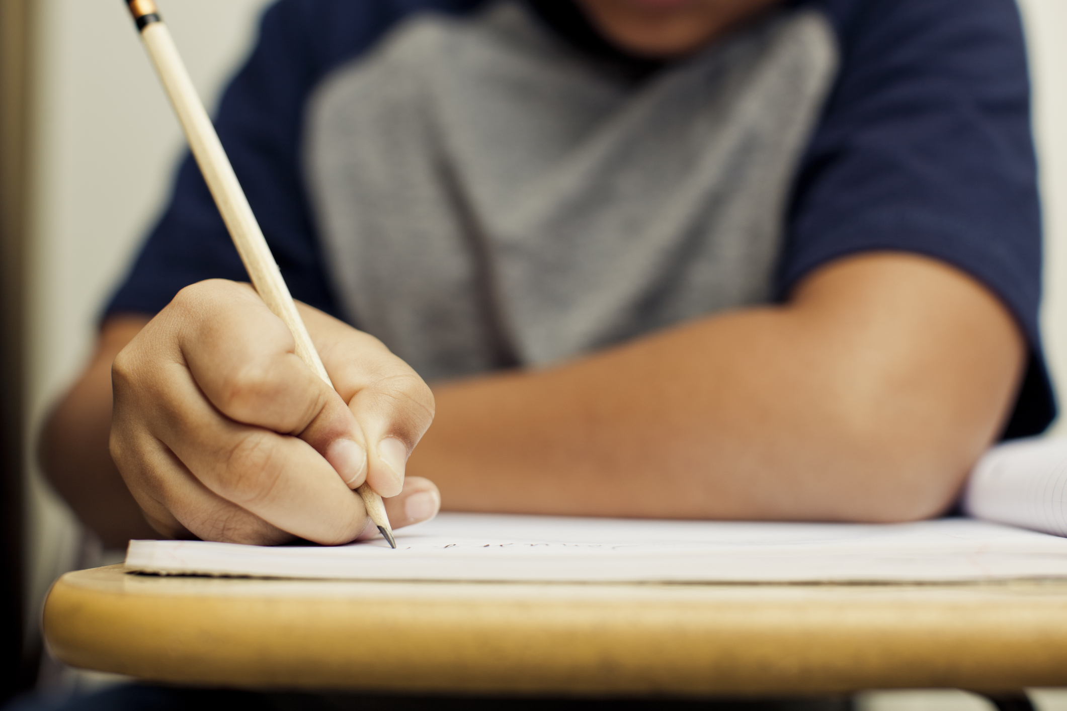Student holds a pencil to a notebook placed on a desk.
