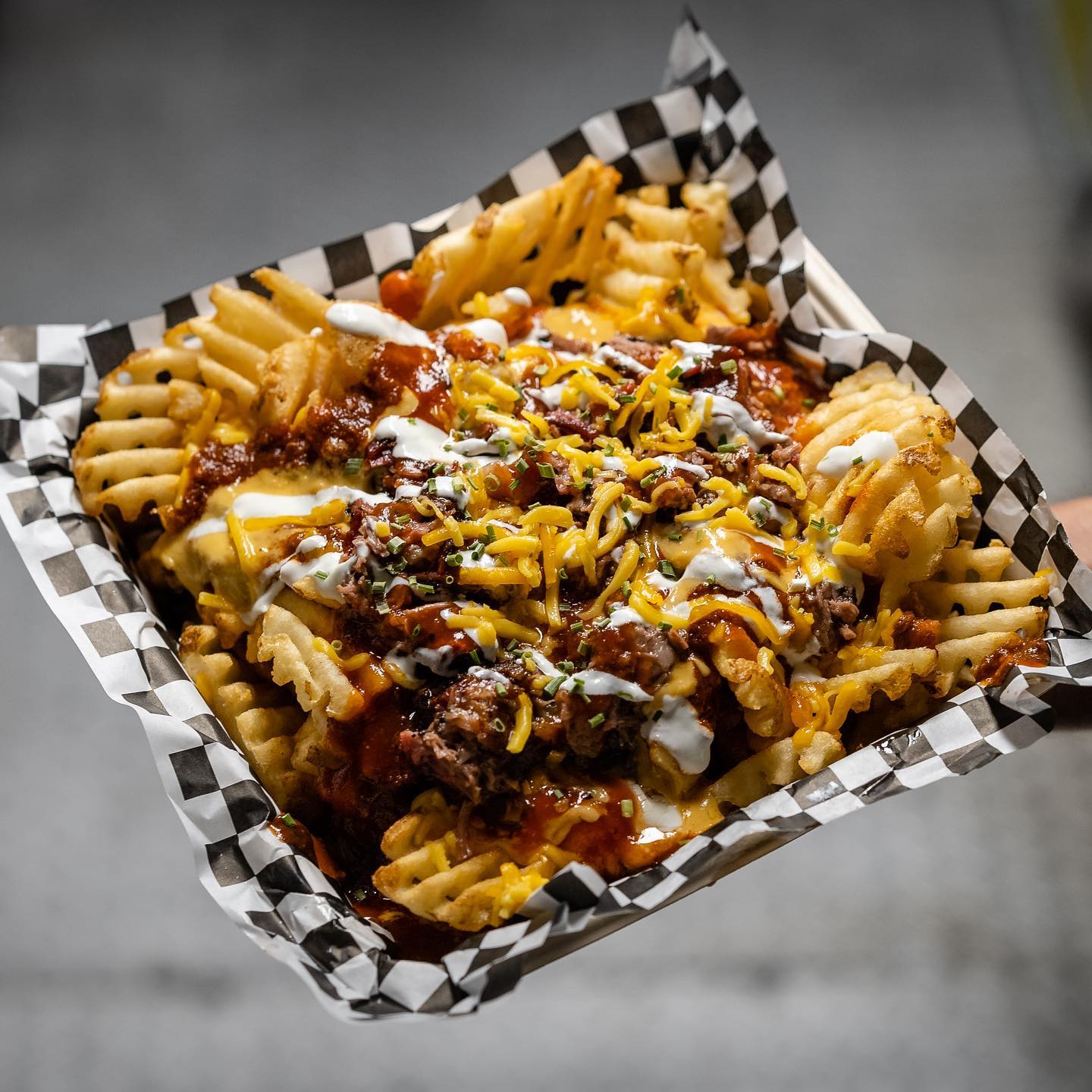 A serving of cheese waffle fries with sauces and brisket tossed in.