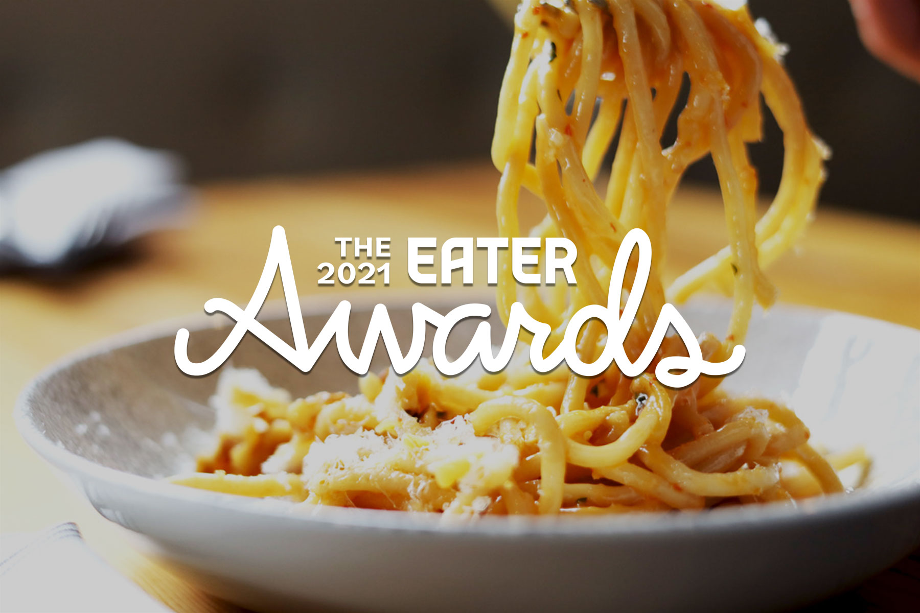 Bucatini pasta lifted off a white plate with a 2021 Eater Awards logo overlayed on the image. 