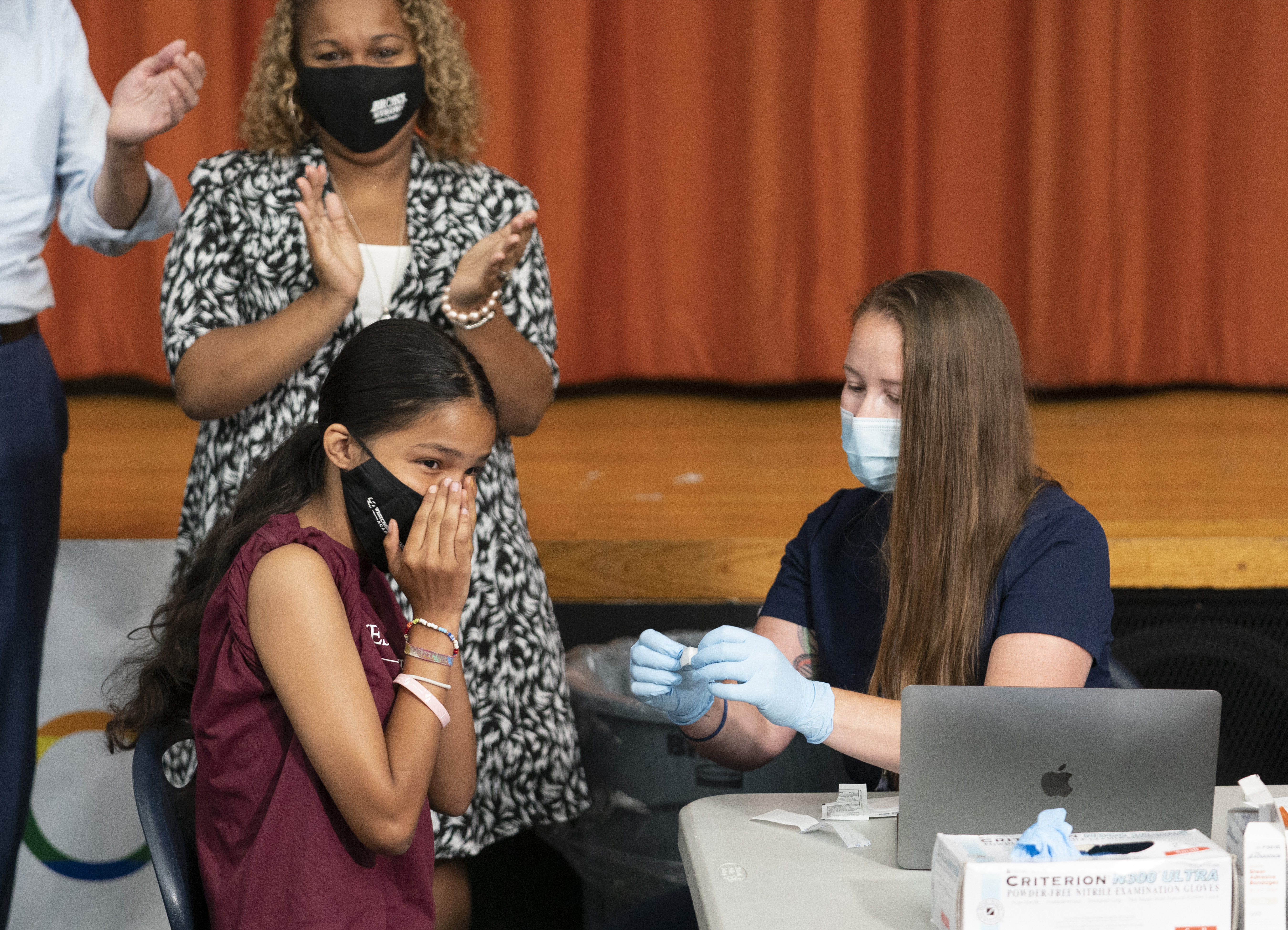 Ariel Quero, 16, left, a student at Lehman High School, reacts after getting the Pfizer COVID-19 vaccine from Katrina Taormina, right, July 27, 2021, in New York. The U.S. is expanding COVID-19 boosters, ruling that 16- and 17-year-olds can get a third dose of Pfizer’s vaccine. 