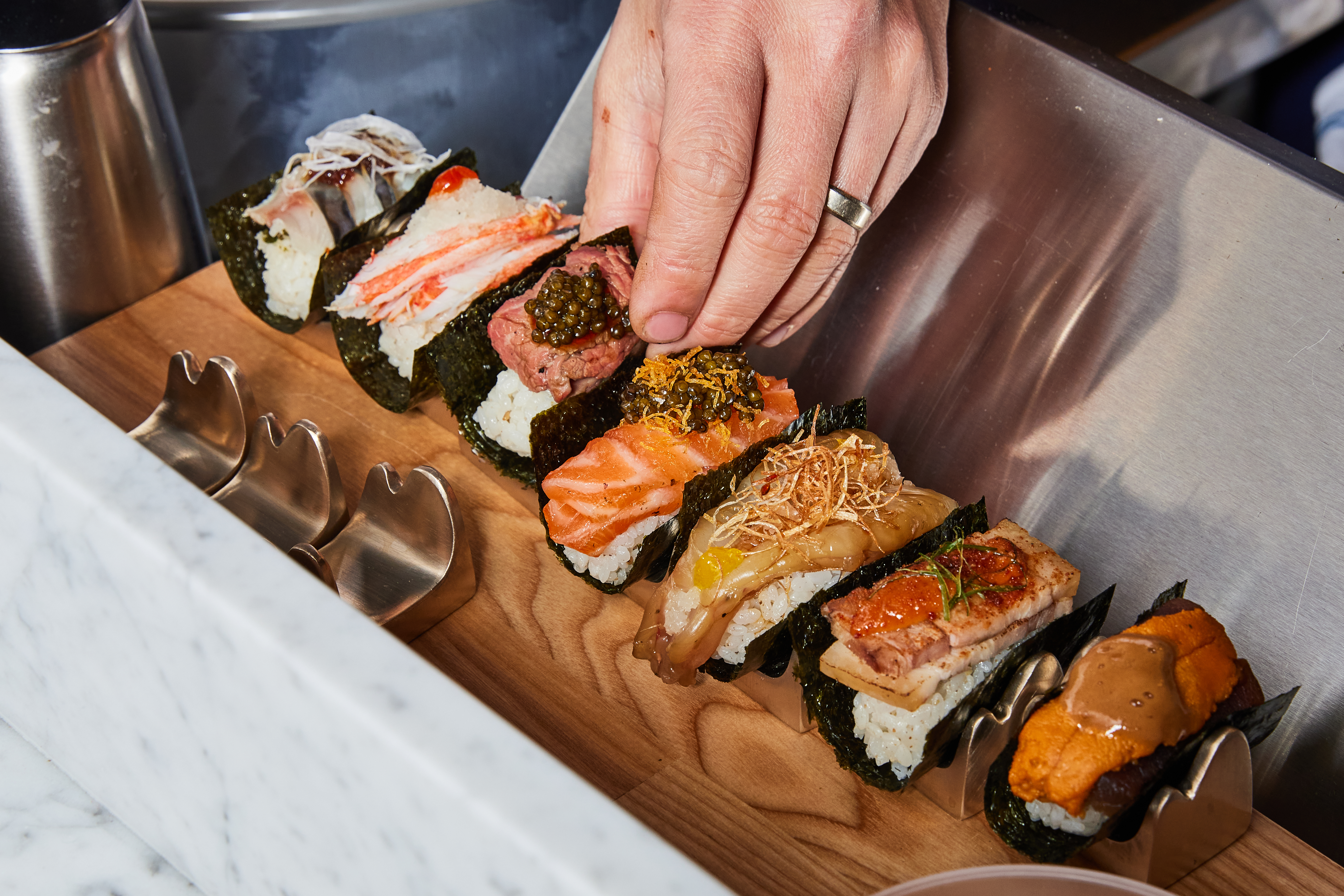 Several handrolls are lined up on a wooden base as a hand reaches in.