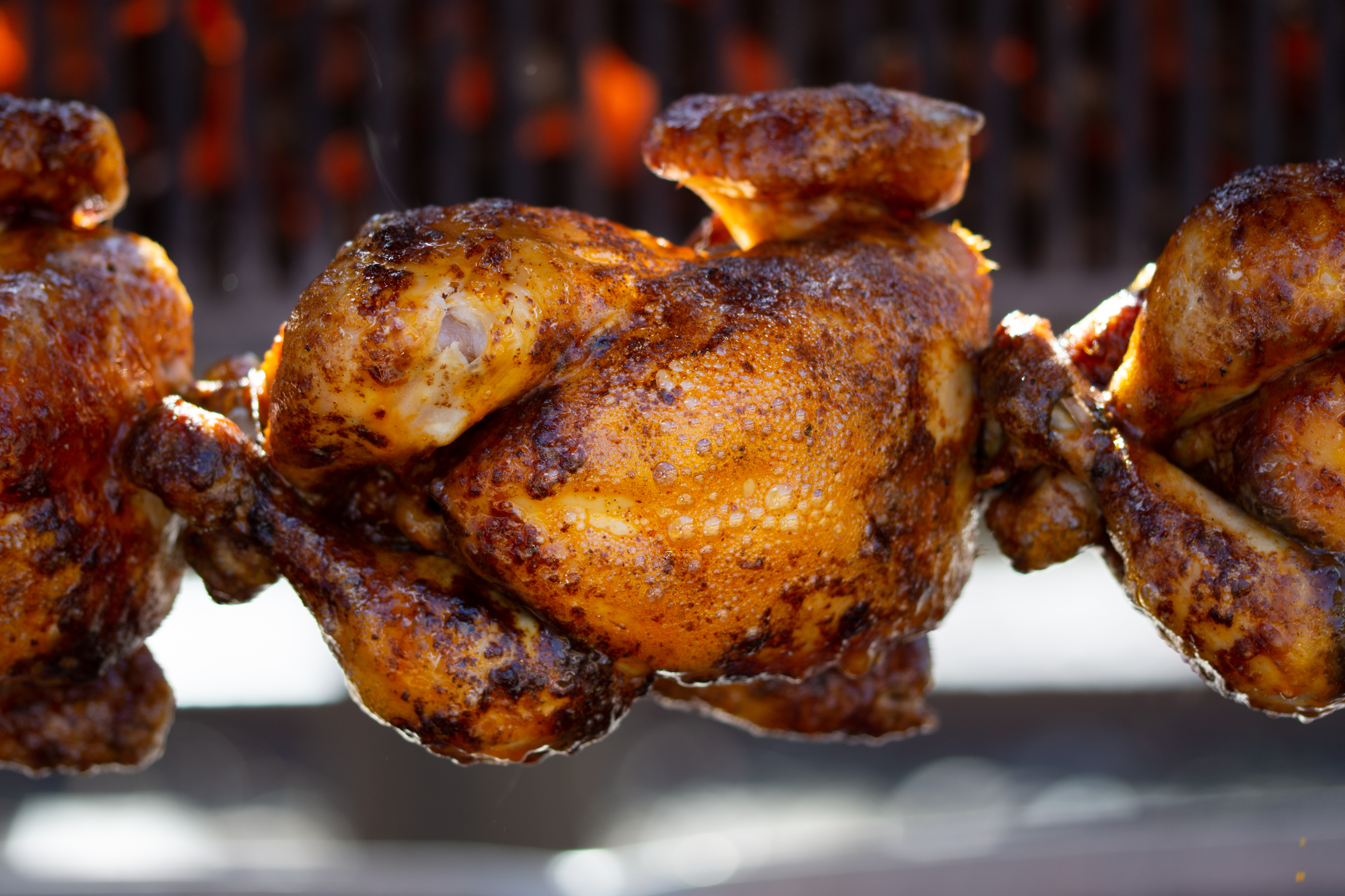 A rotisserie chicken on a spit between two other rotisserie chickens