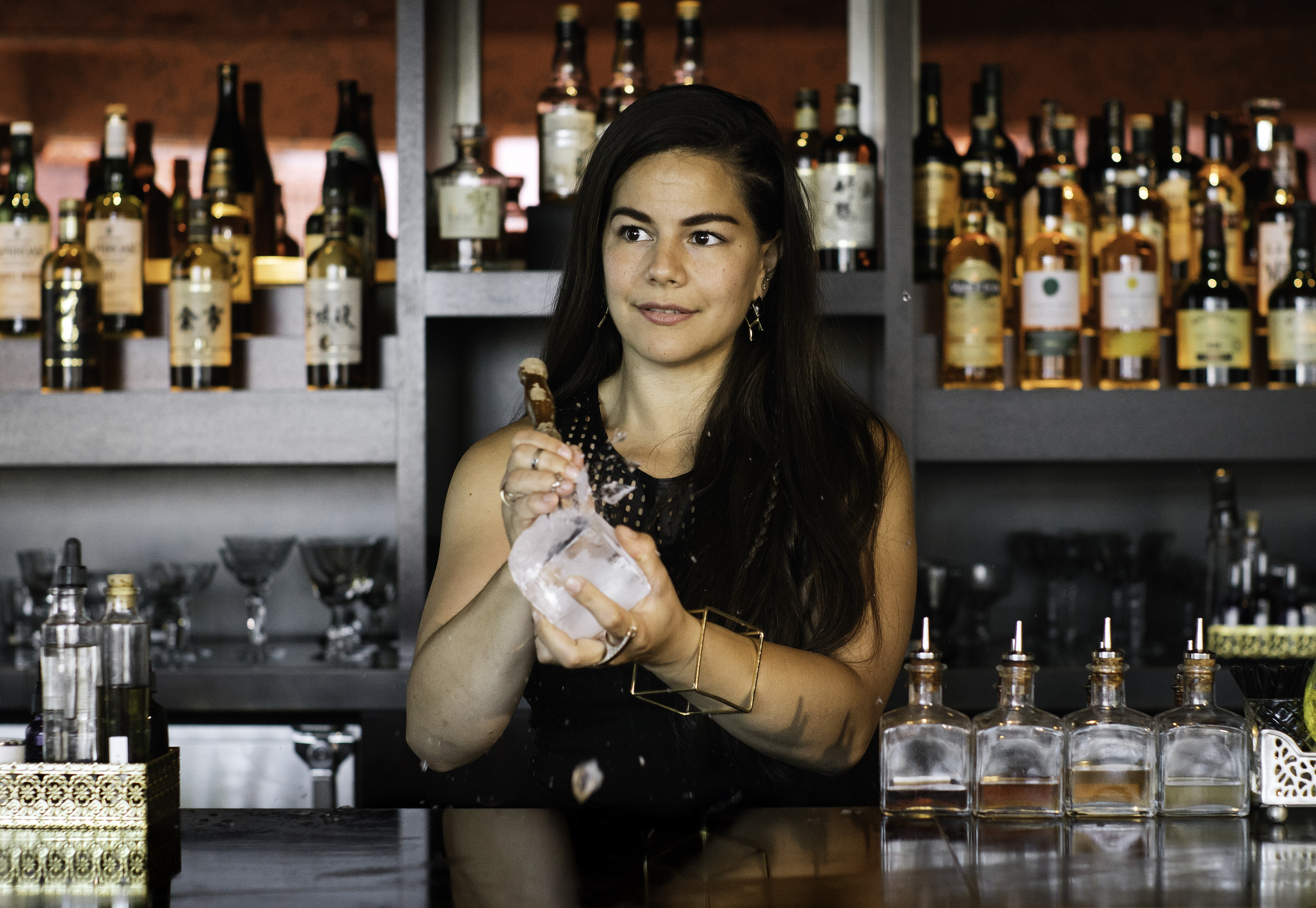 A woman stands behind a bar holding a cocktail shaker
