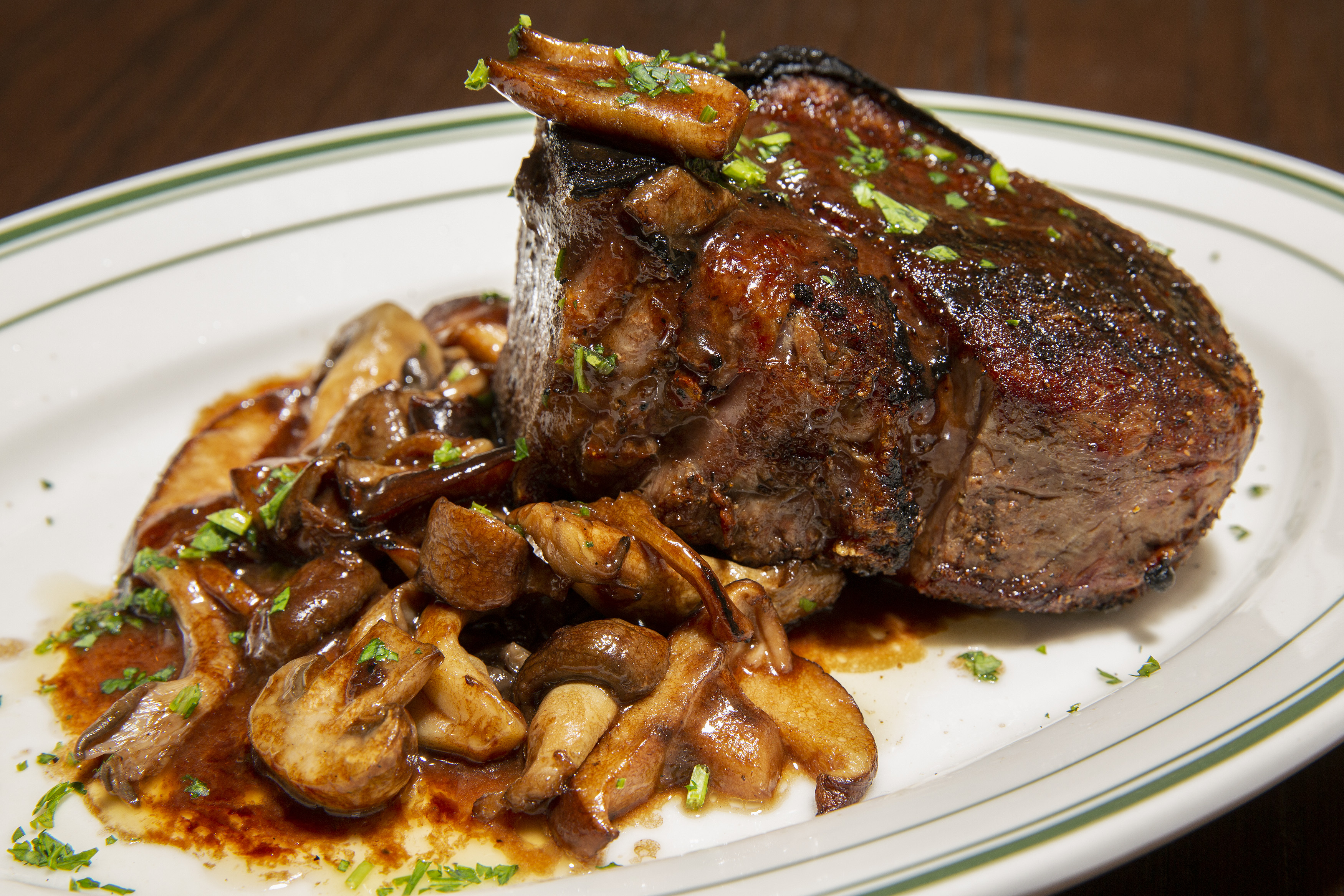 A juicy-looking filet mignon beside a pile of browned mushrooms on a white plate.