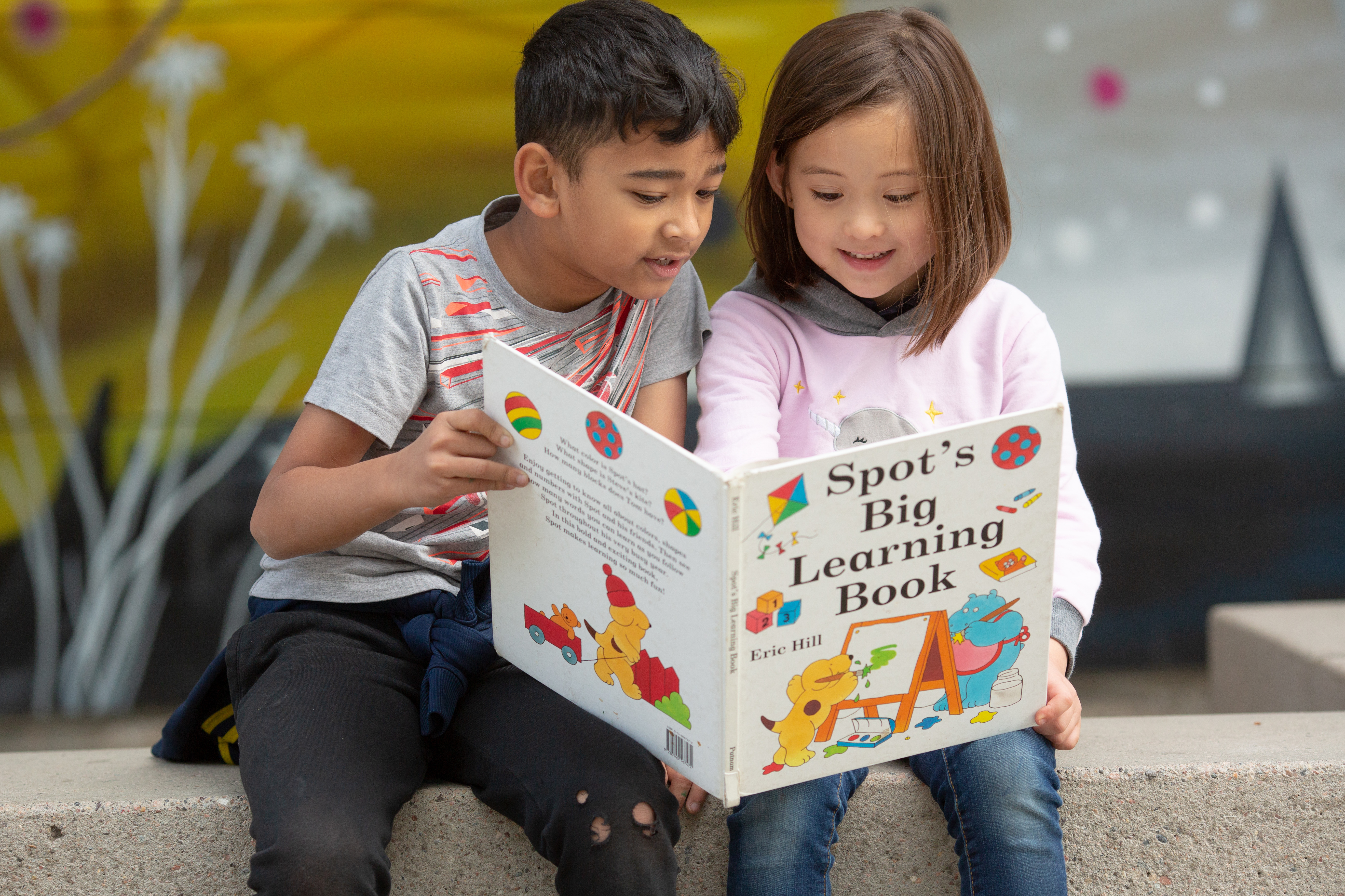 A young girl and boy sit together reading a book called “Spot’s Big Learning Book.”