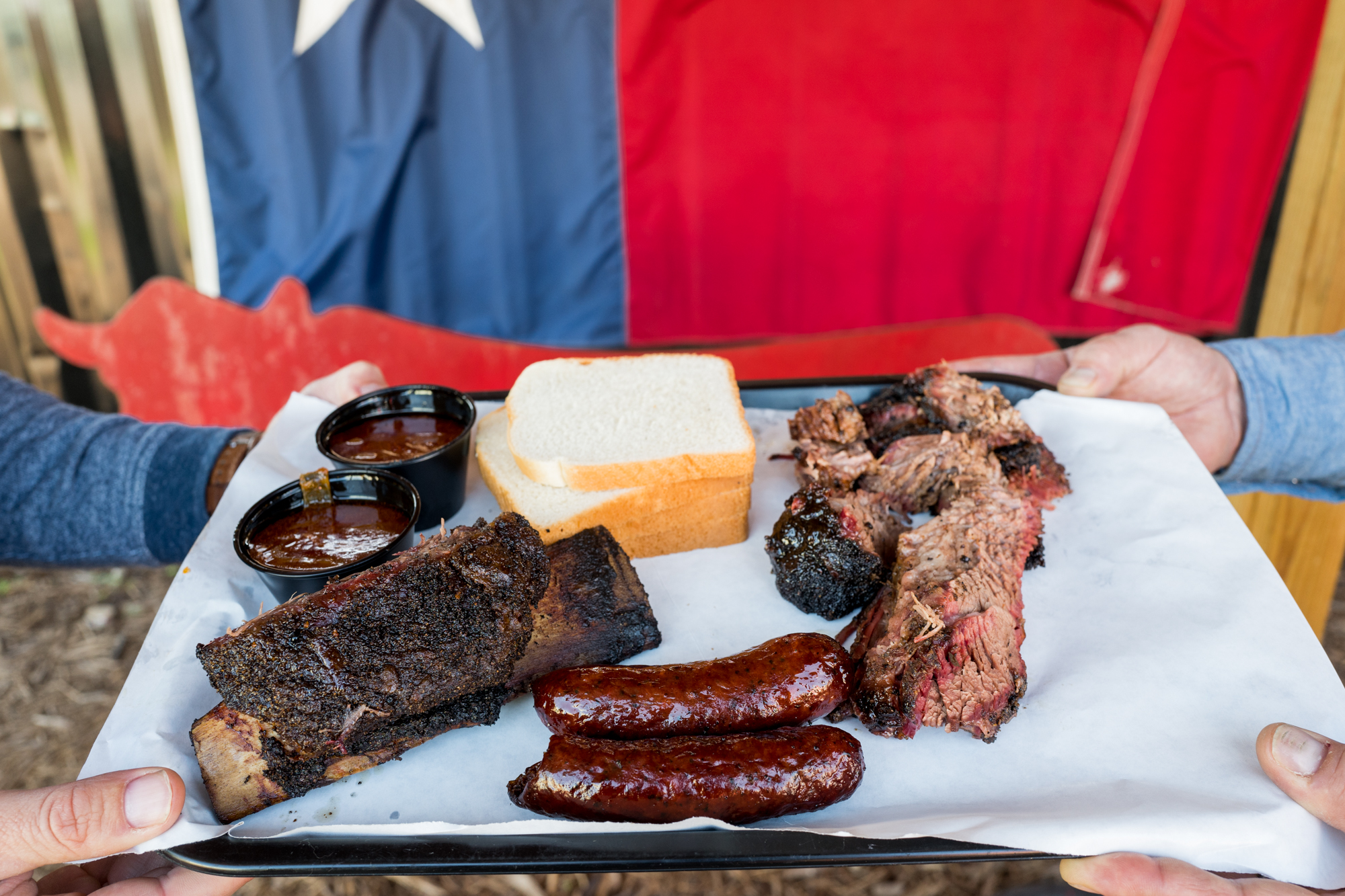 A tray of barbecued meats in front of a Texas flag.