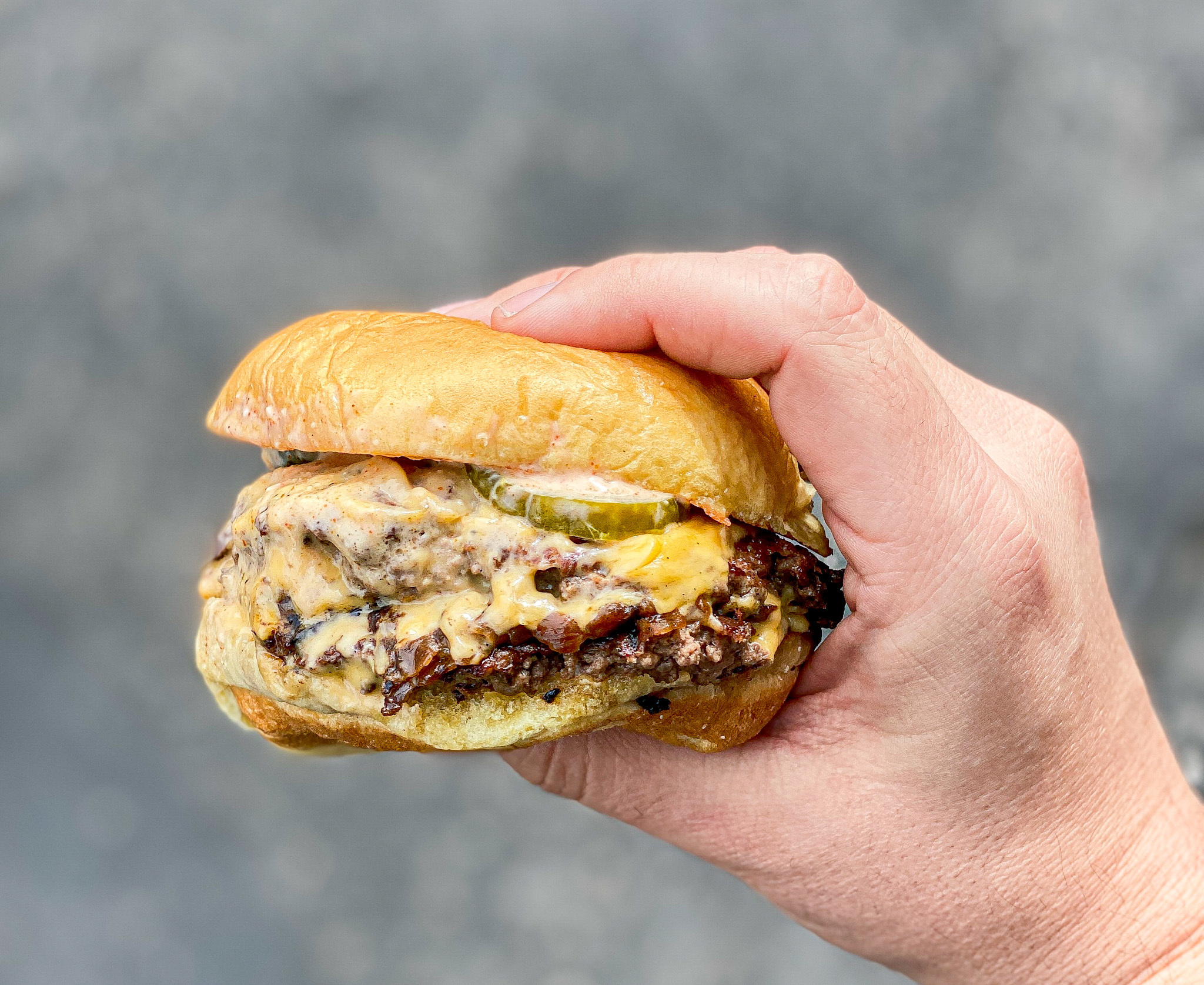 A hand grips a cheesy double patty burger.