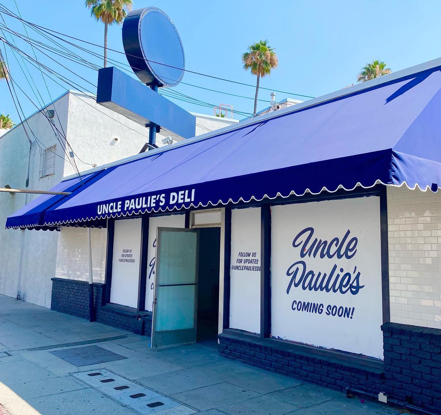 A daytime exterior of a blue deli restaurant with white tones.