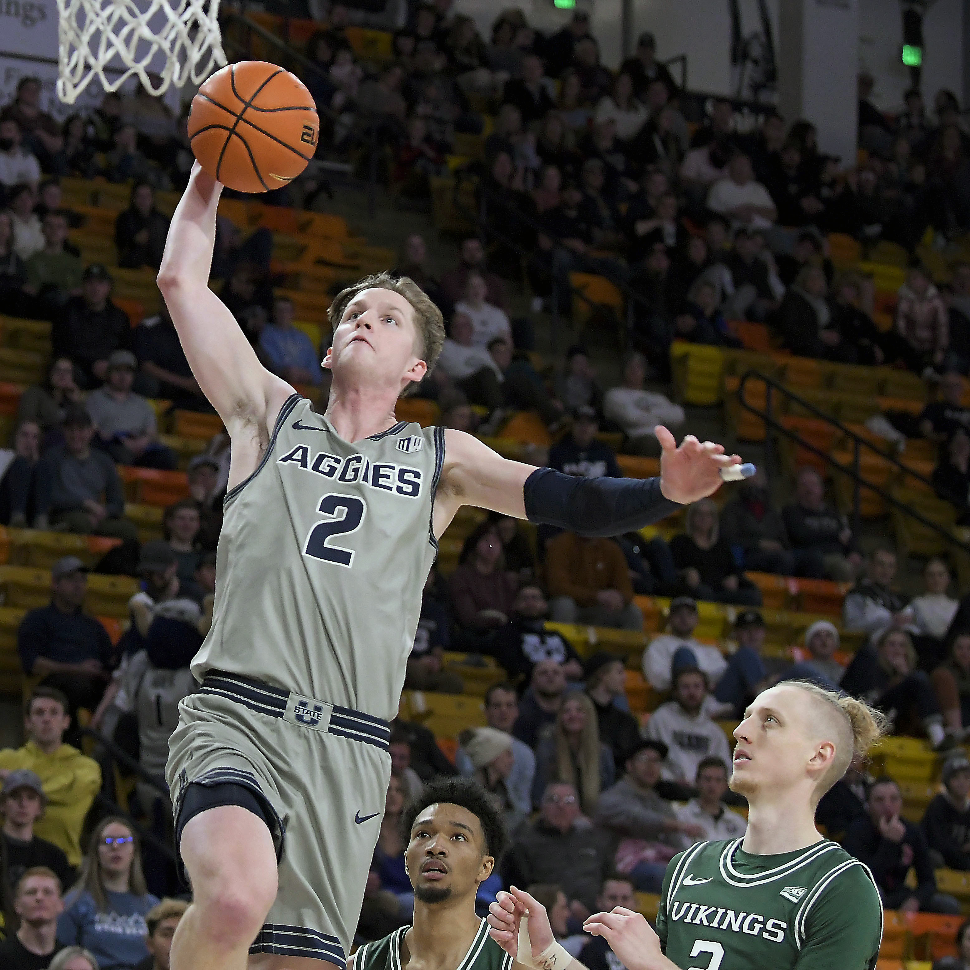 Utah State guard Sean Bairstow, wearing grey, goes up to dunk the ball as Portland State guard Michael Carter III and guard Ian Burke defend.