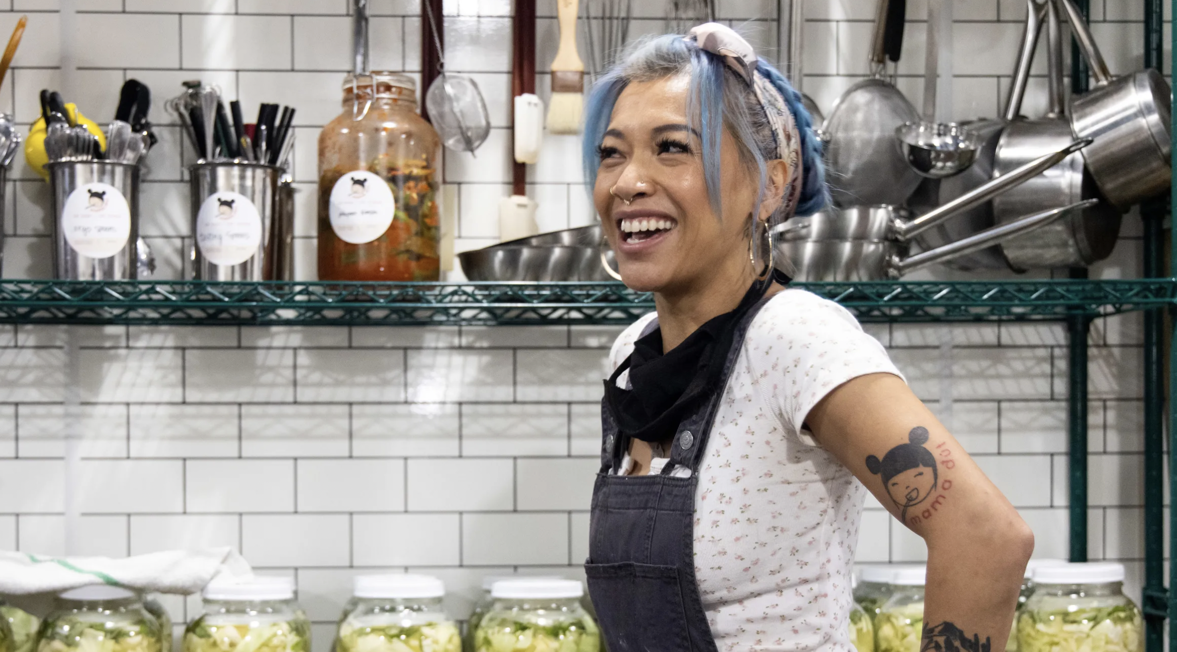 Mama Dút owner Thuy Pham stands in front of a white tile wall hung with kitchen racks