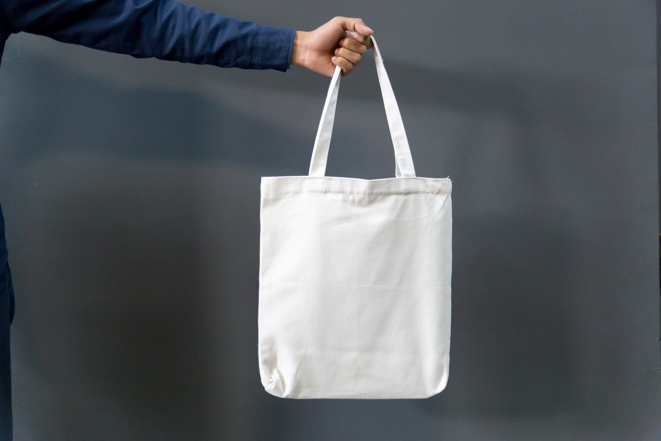 A person’s hand holding a blank fabric tote bag.