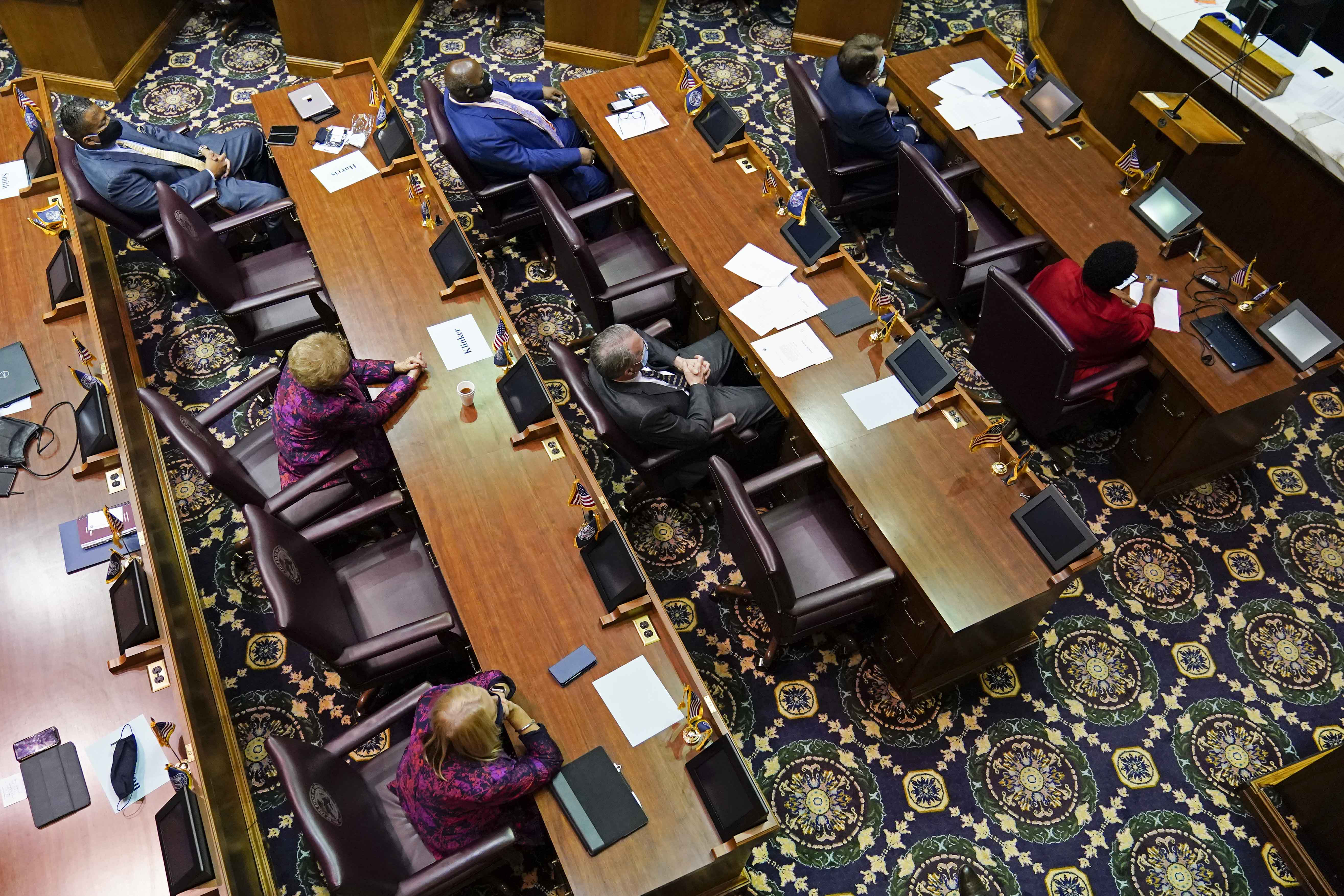 View looking down on the floor of the Indiana House, with people sitting at desks, separated by empty seats