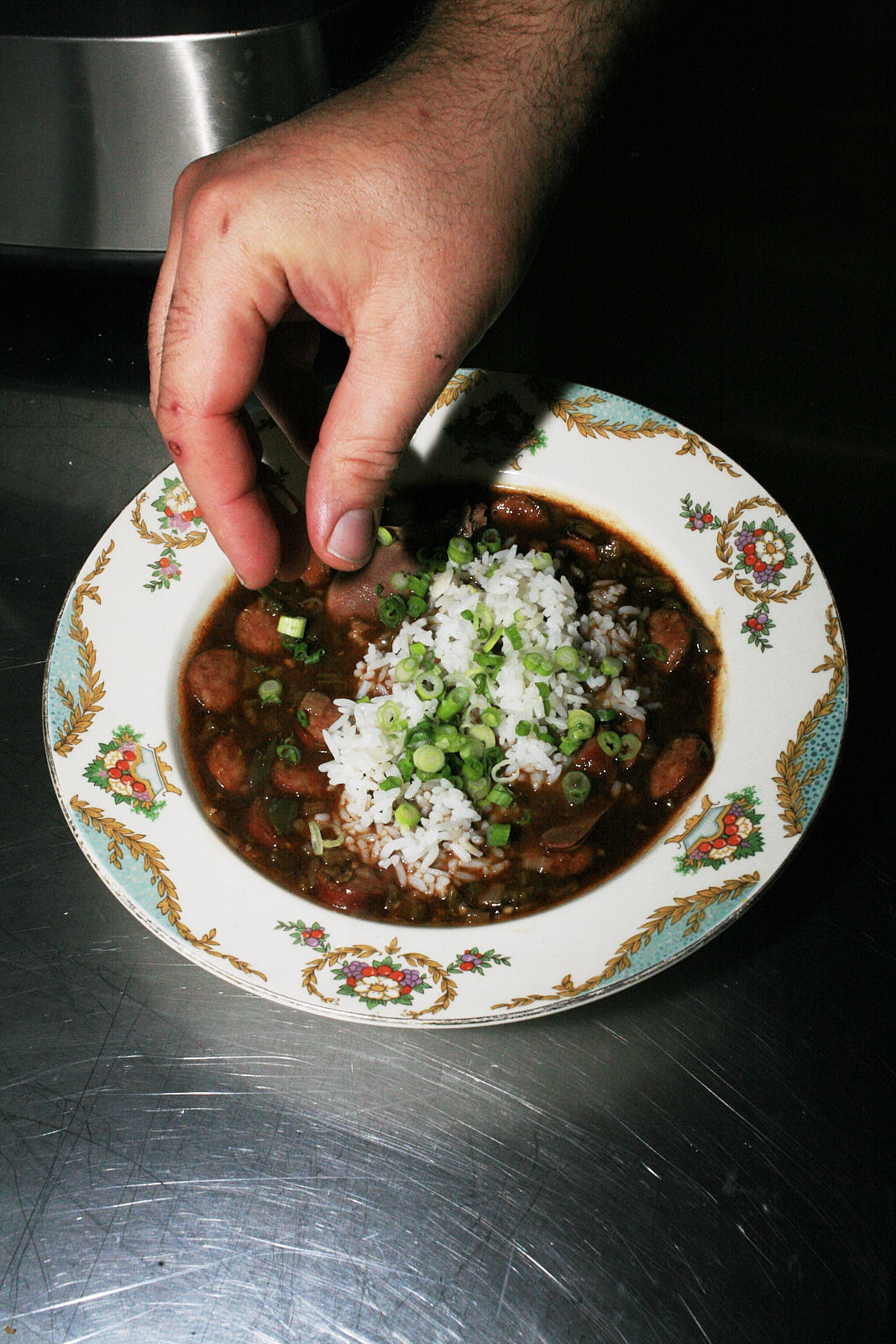 A shallow, floral-patterned china bowl of the gumbo, now with white rice and spring onions added.
