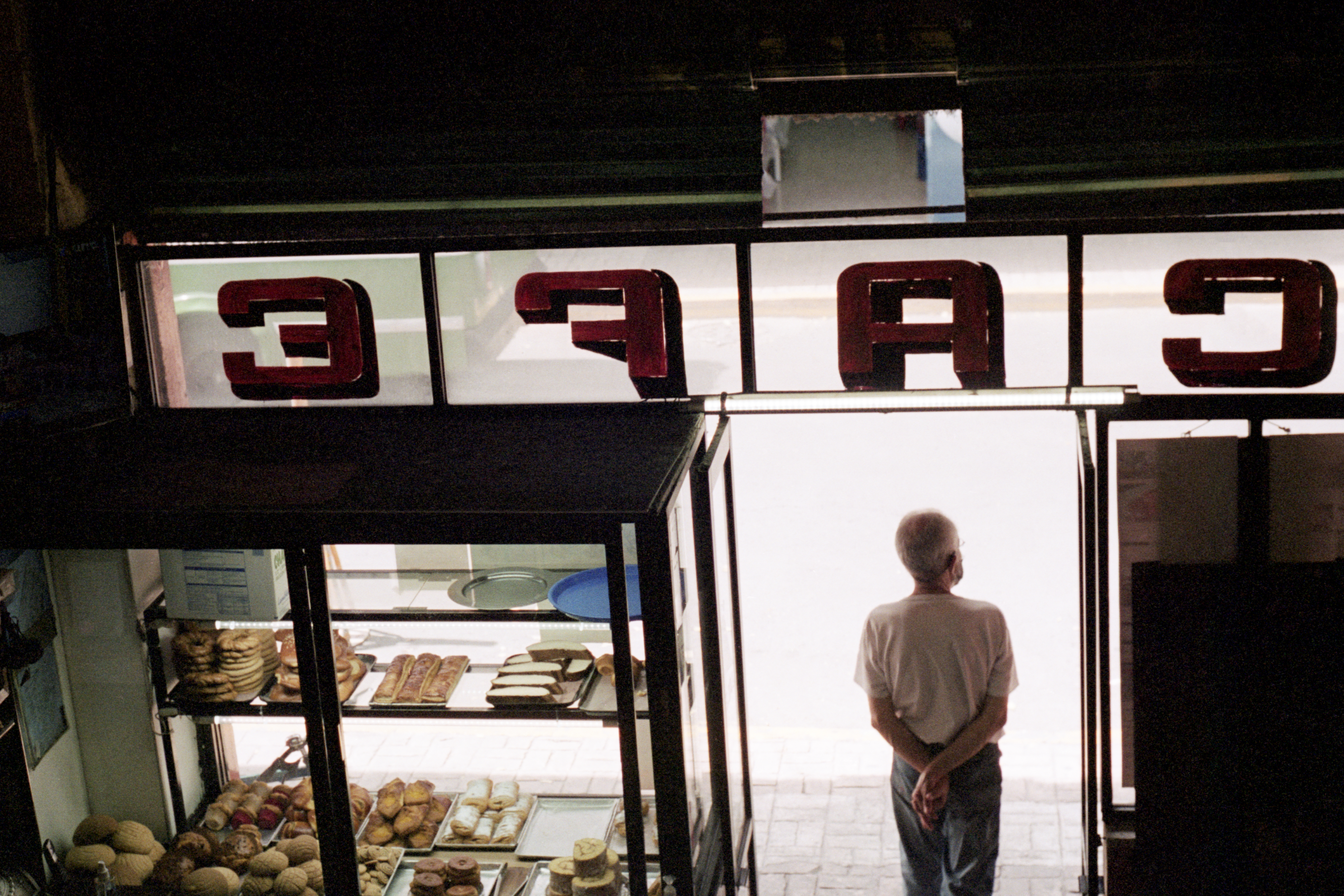 A man looks out the doorway longingly with a display of pastries in the shop window next to him. 
