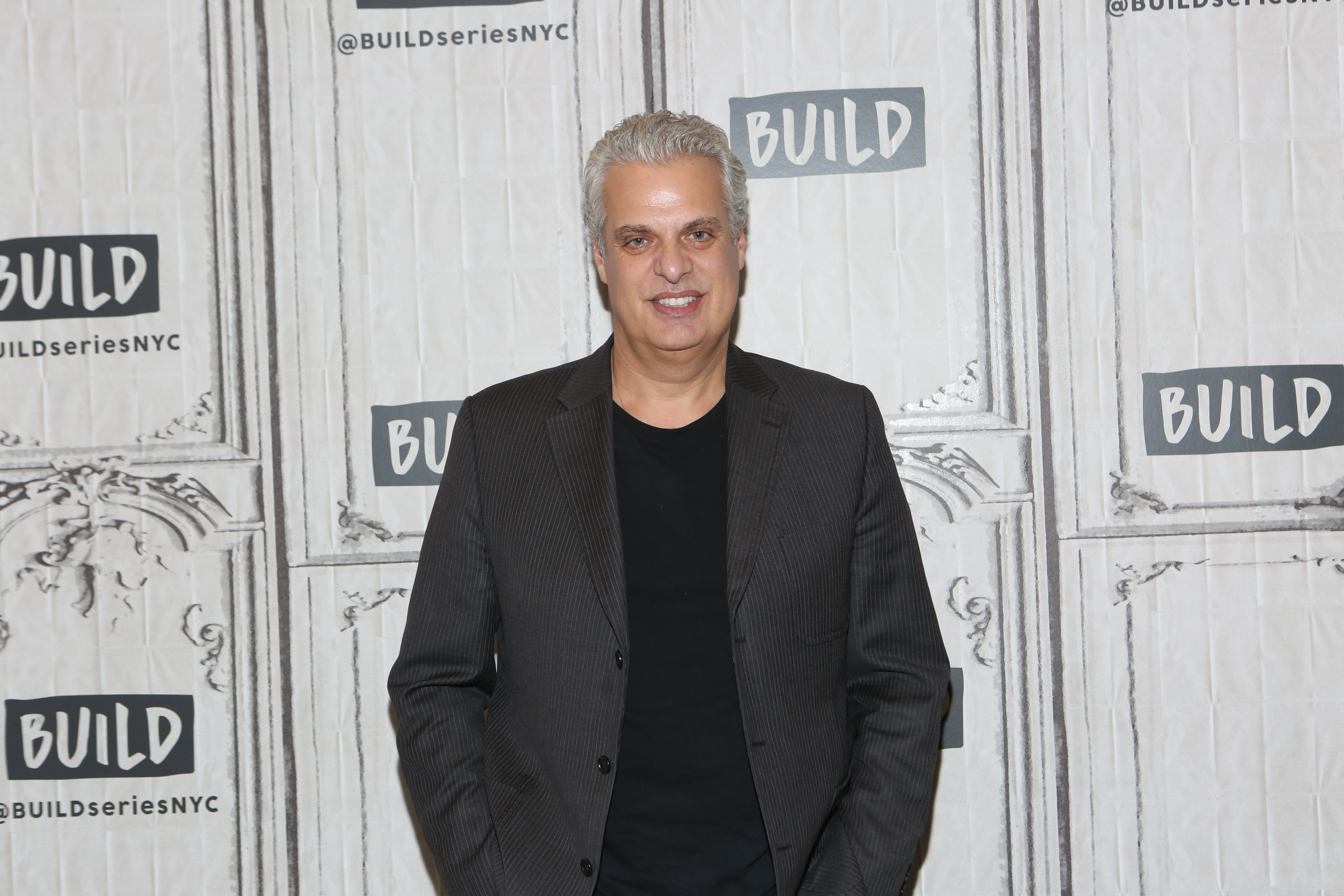 Chef Eric Ripert in a black t-shirt and jacket, standing and smiling at the camera.