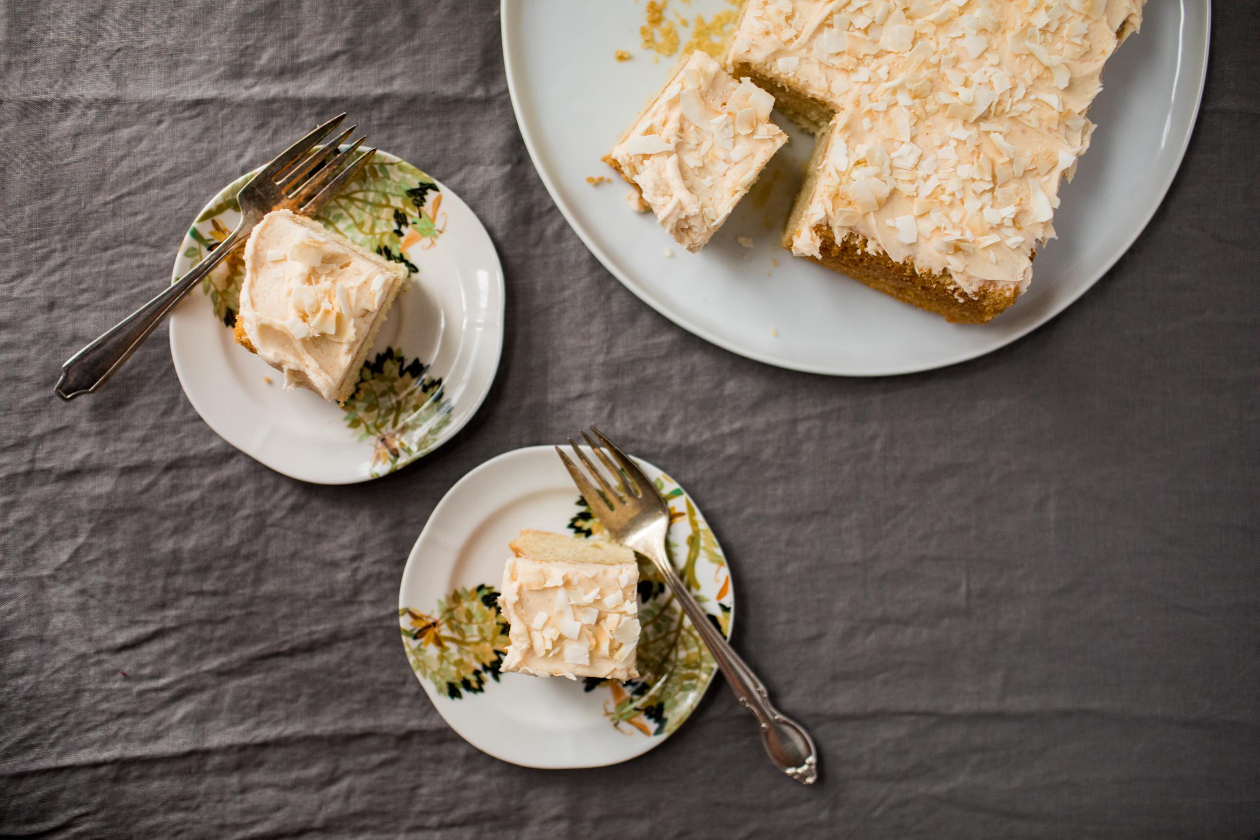 Two squares of key lime cakes are served on small plates. The rest of the cake sits next to them on a large platter.