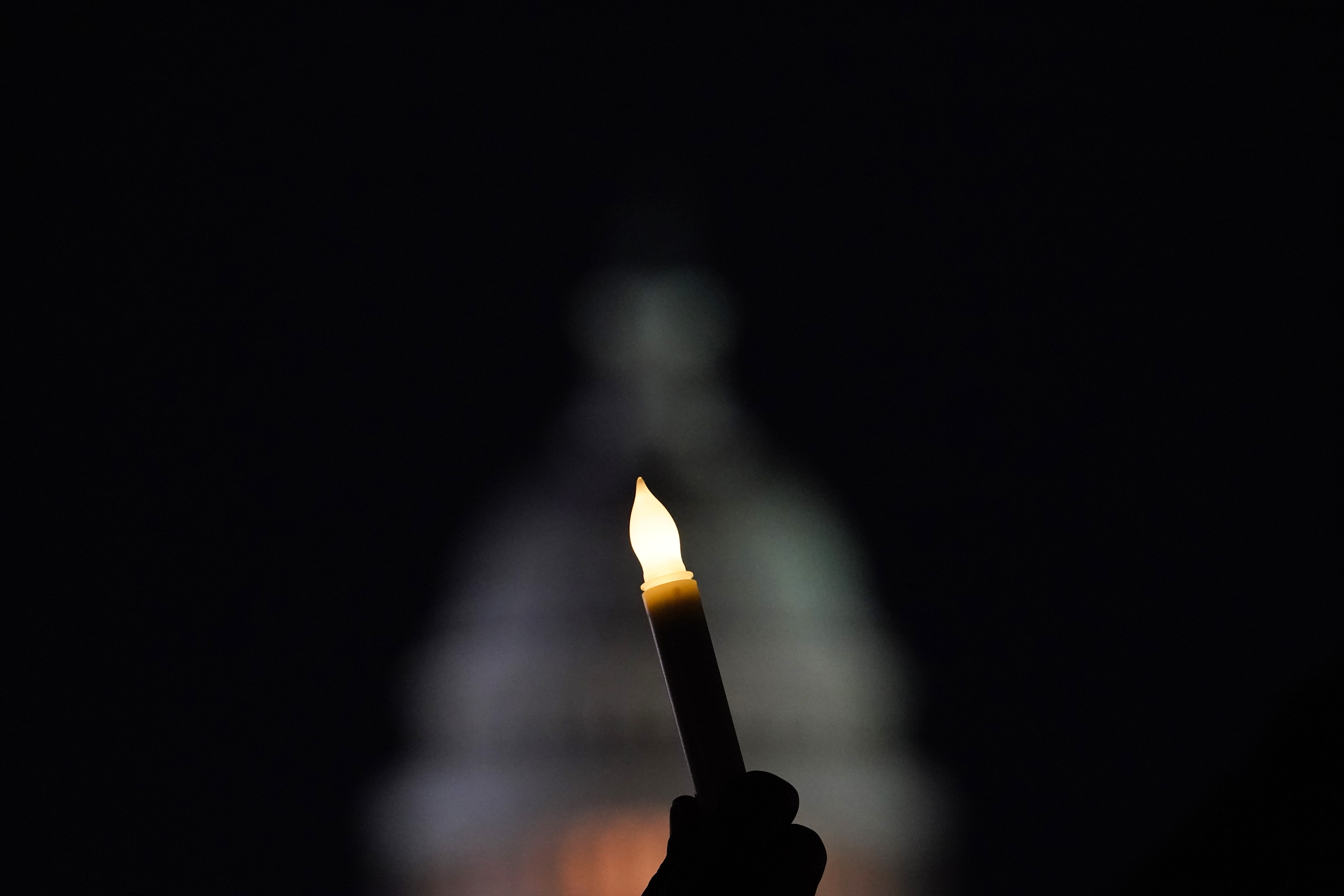 With the U.S. Capitol in the background, a person holds a candle at a vigil on the one-year anniversary of the Capitol attack.