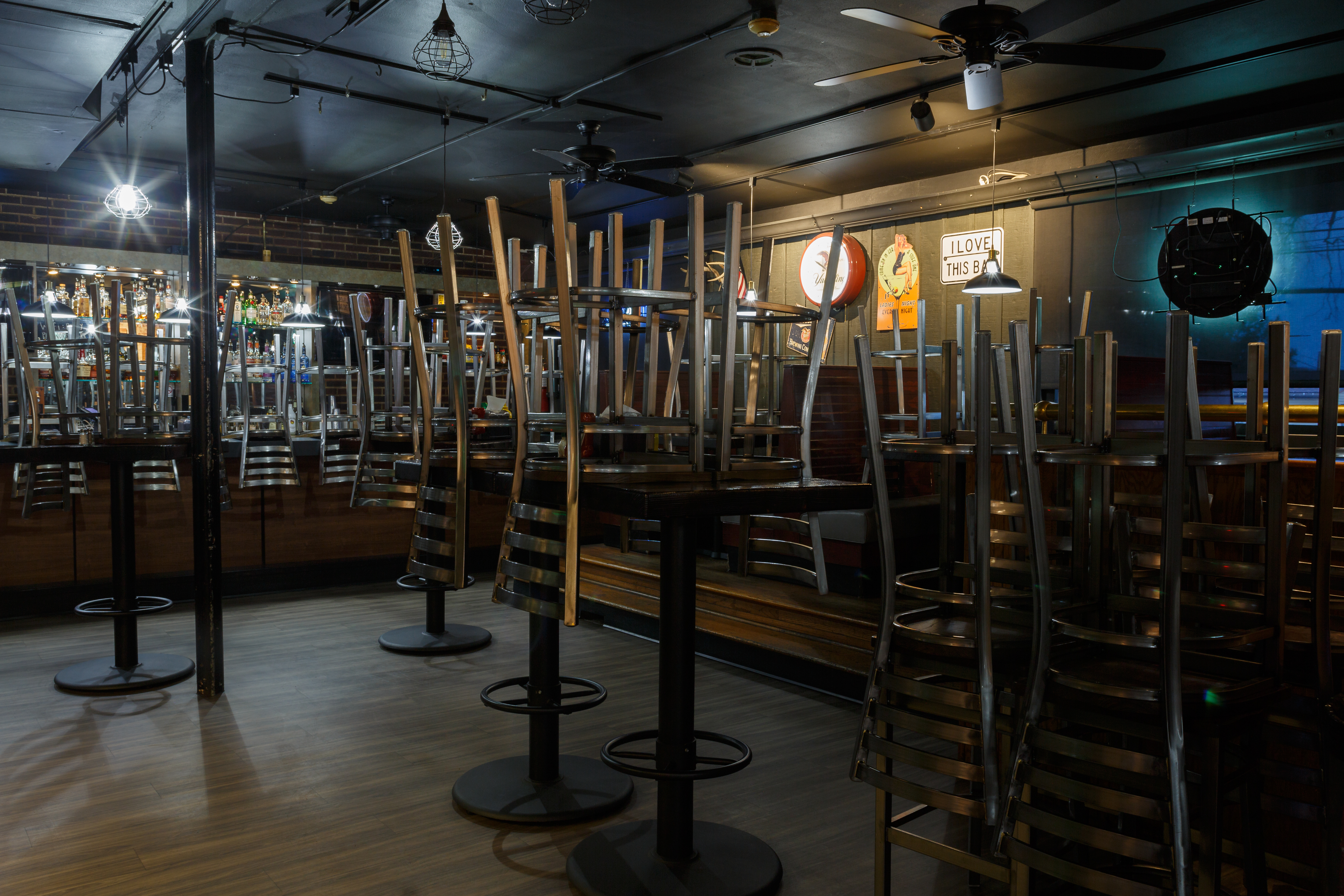 A closed bar is pictured with stools and seats upturned on tables.