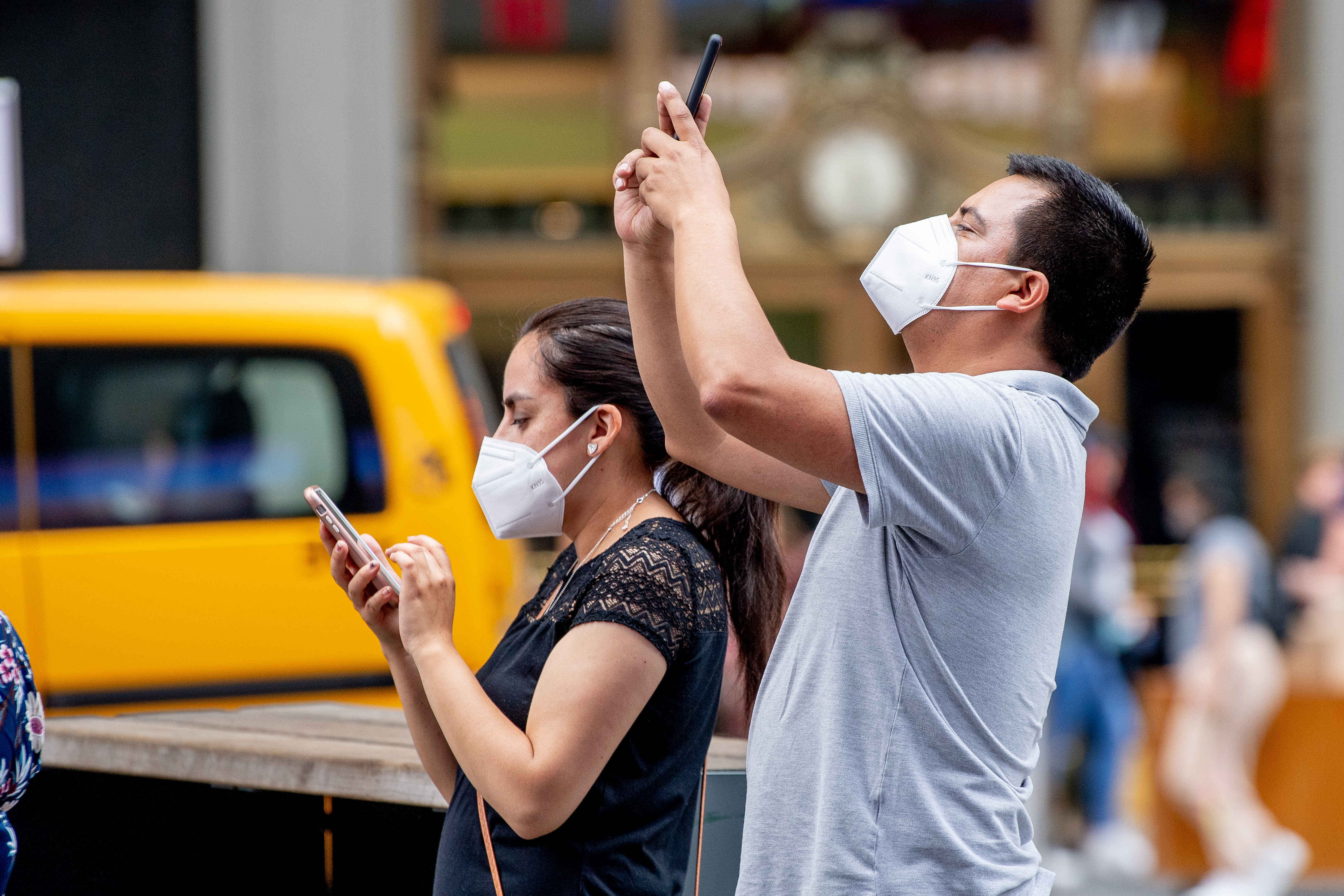 Two people holding phones wear KN95 masks in Times Square, New York City.