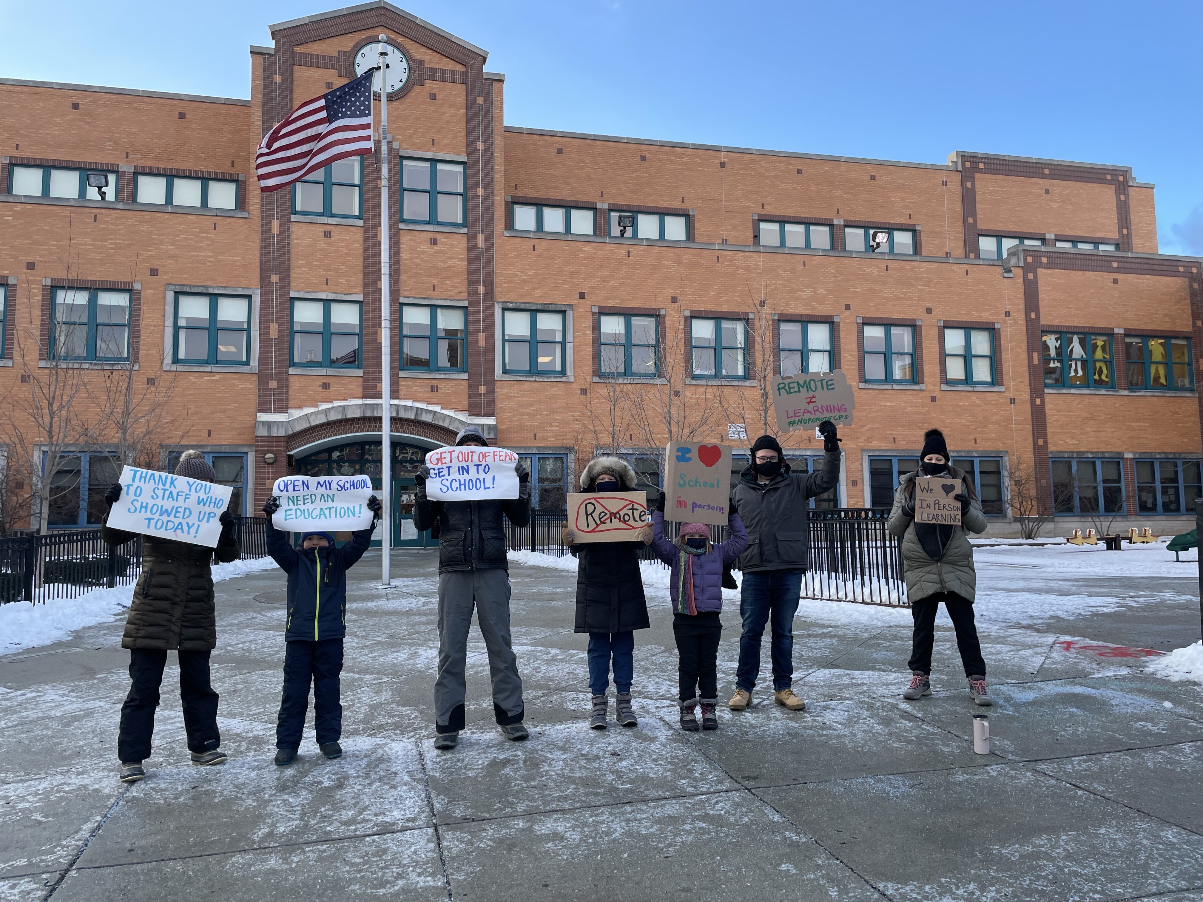 People dressed in winter coats hold signs in front of a school building in Chicago.