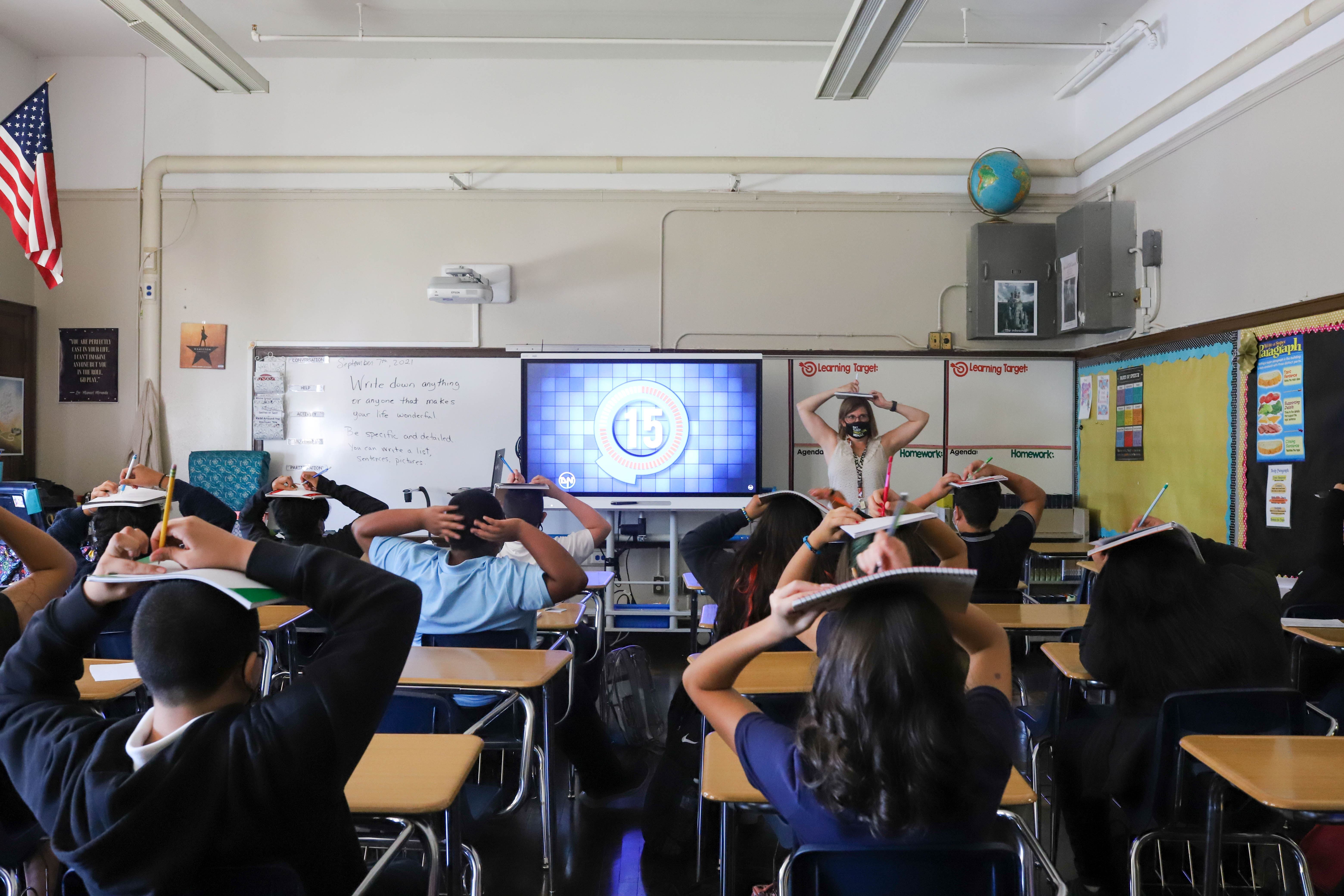 Students and their teacher balance their notebooks on their heads during class on the first day of school.