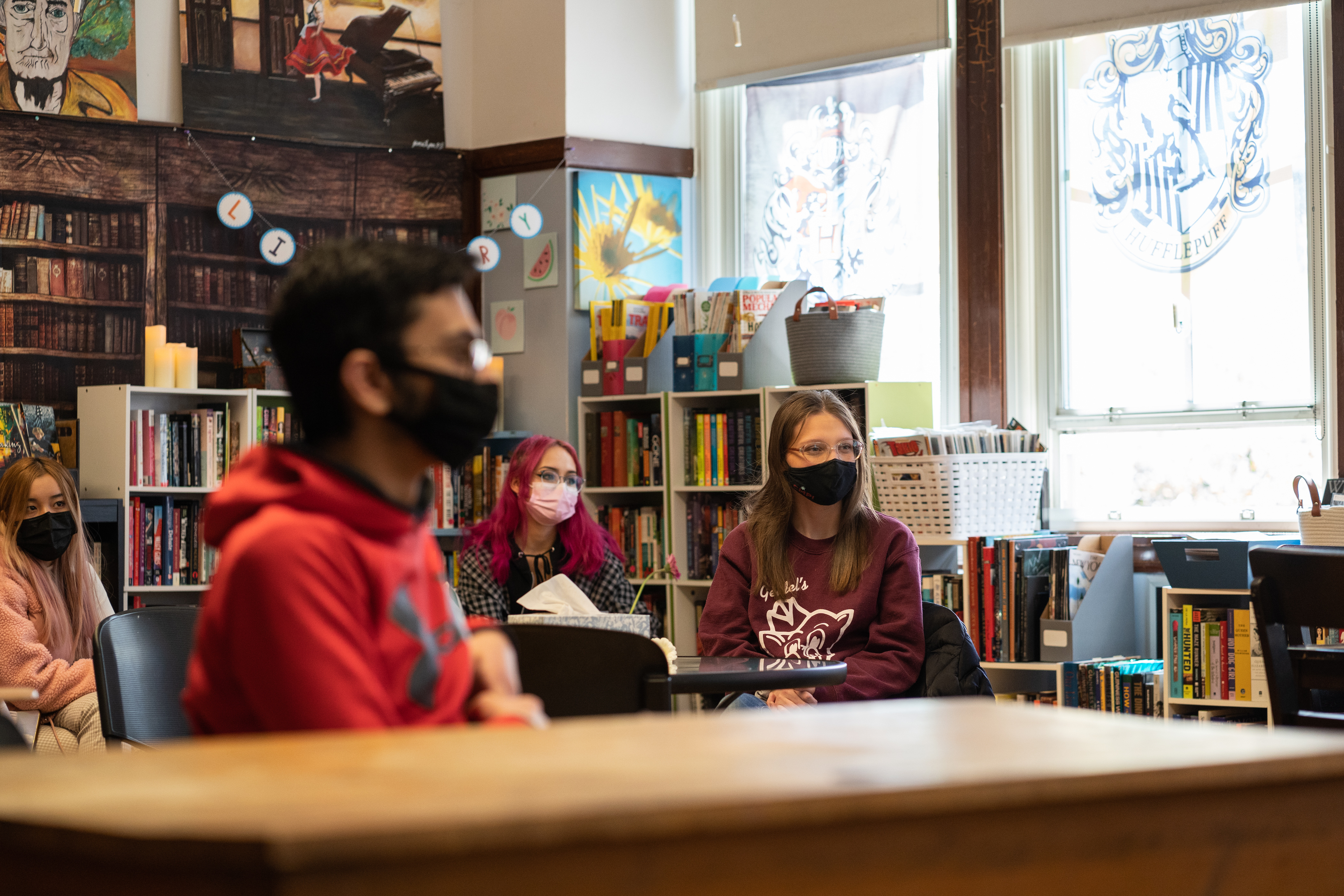 Students discuss plans in class, sitting in distanced desks wearing protective masks.