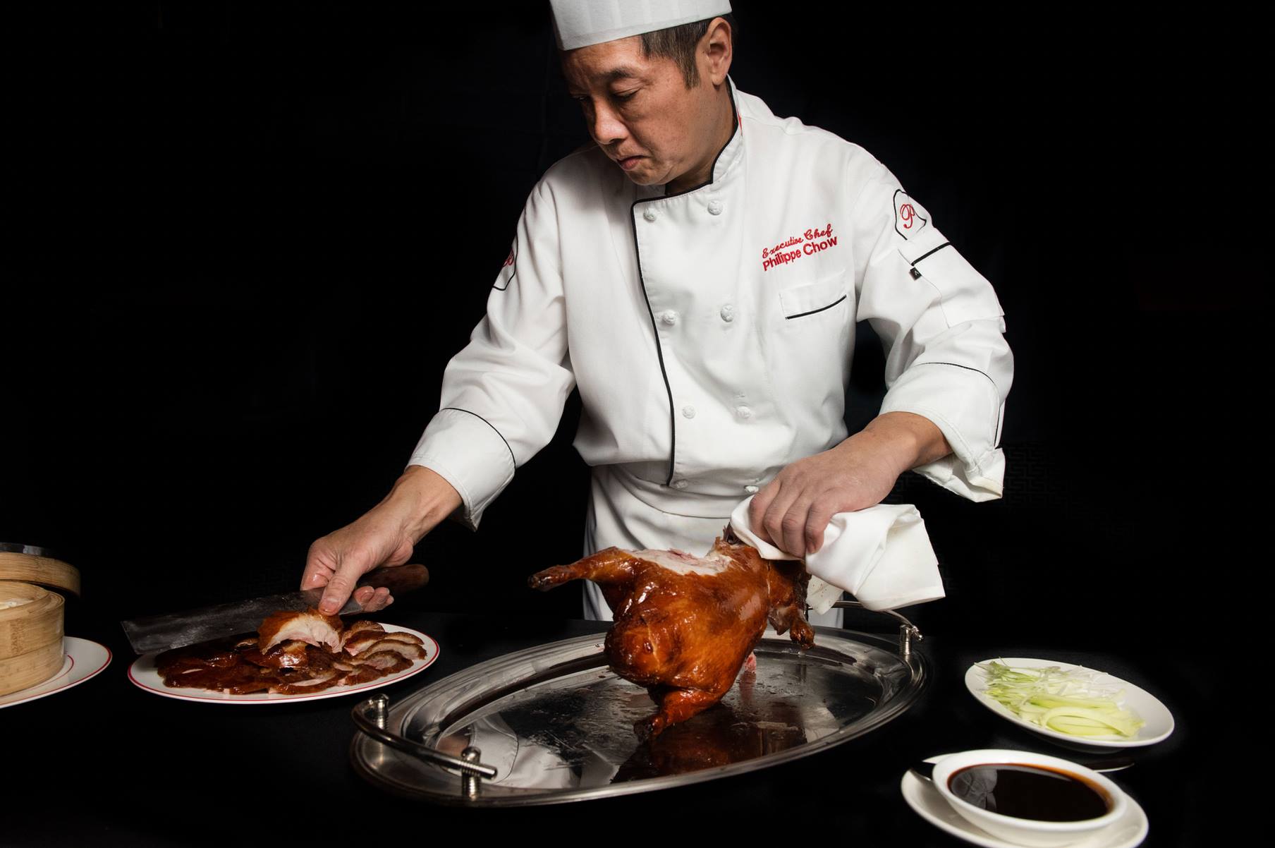 Philippe Chow preparing duck in a white chef jacket.