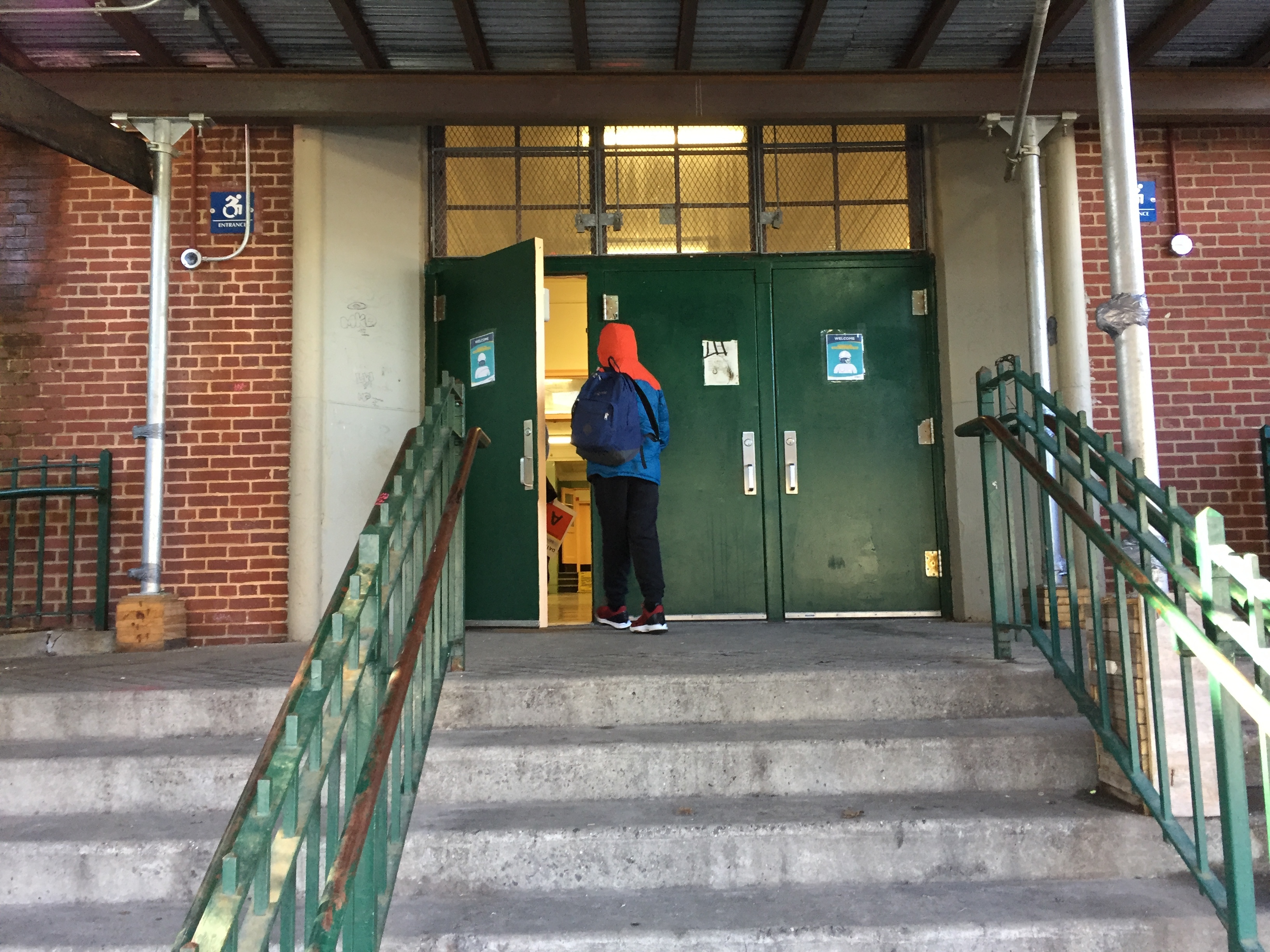 Students at M.S. 51 in Park Slope, Brooklyn walk into the building, socially distanced and masked. The foreground is steps and a green railing.